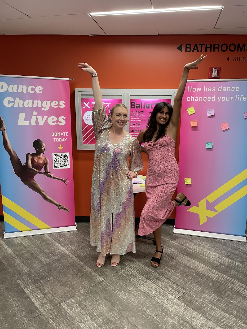 Ayesha Patel standing with another person, both of their arms raised up, in front of posters saying Dance Changes Lives and How has dance changed your life and BalletX