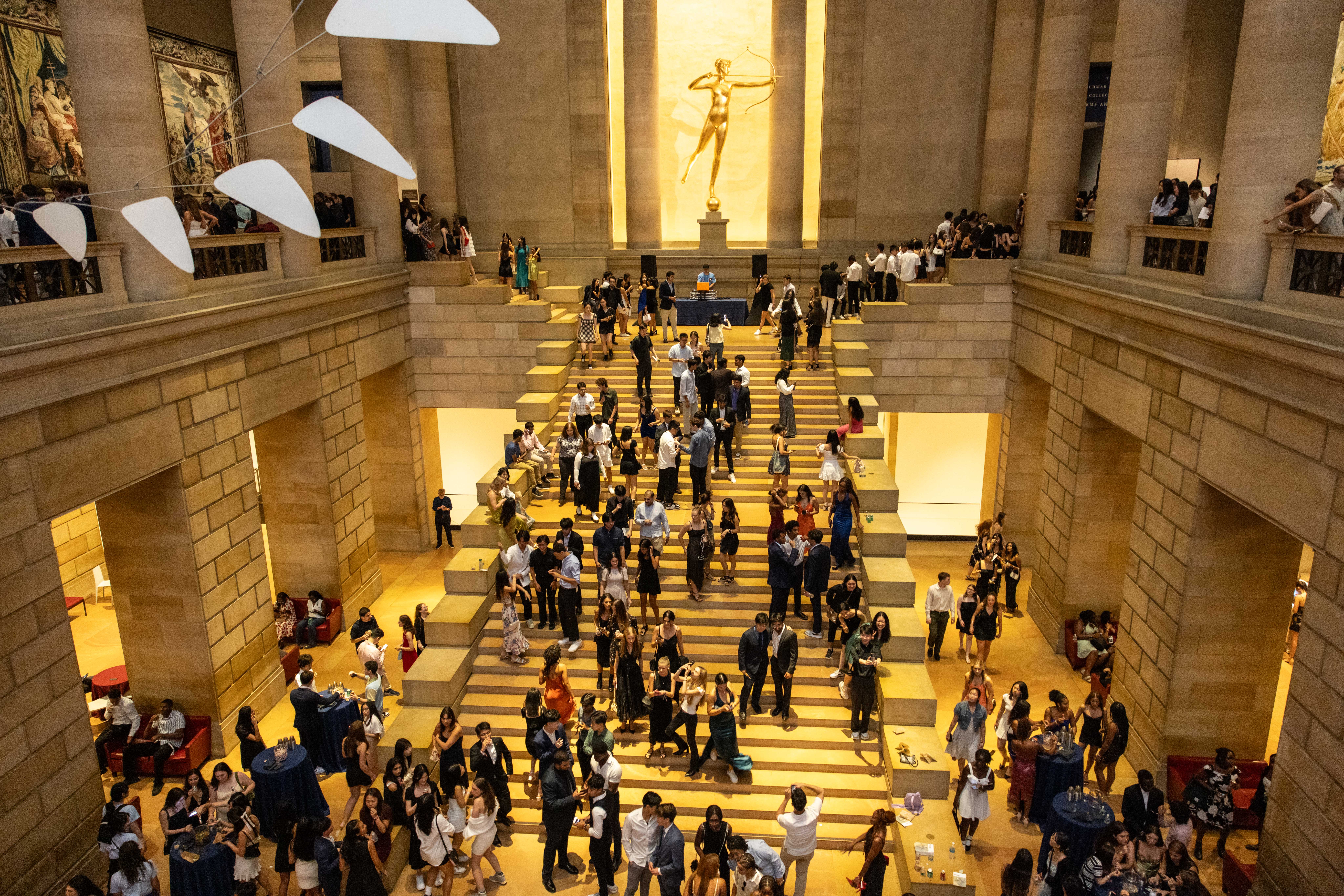 Students mill about on the Great Stair Hall in the interior of the Philadelphia Museum of Art. A gilded statue of Diana as an archer is in the background; Calder's Ghost mobile sculpture is in the foreground