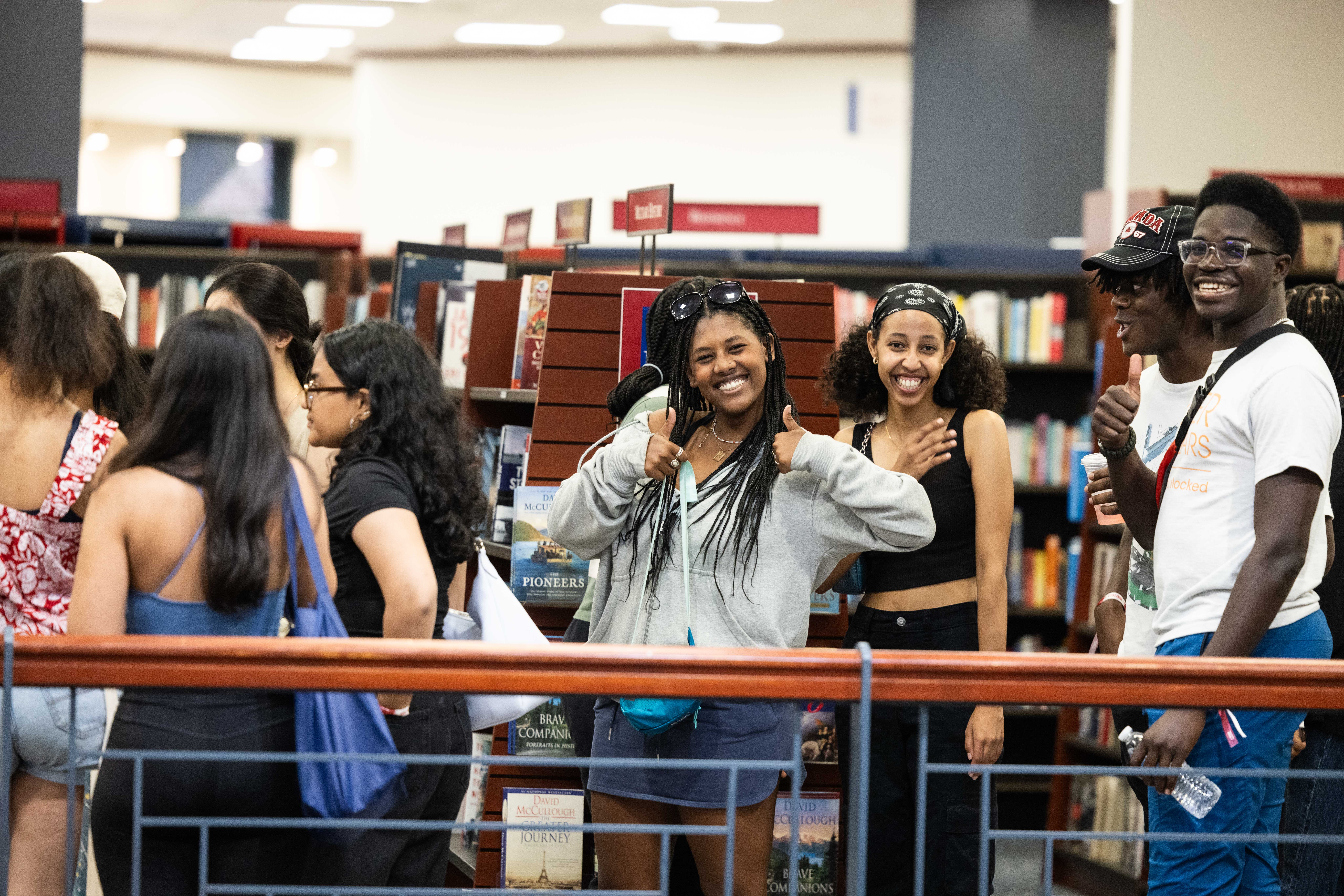 Students smile and give a thumbs up while waiting in line at the bookstore