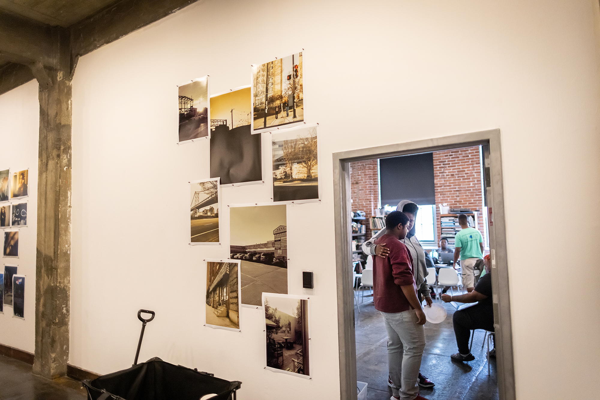 A hallway with mounted, overlapping photographs opens up to a classroom where the Sayre students work
