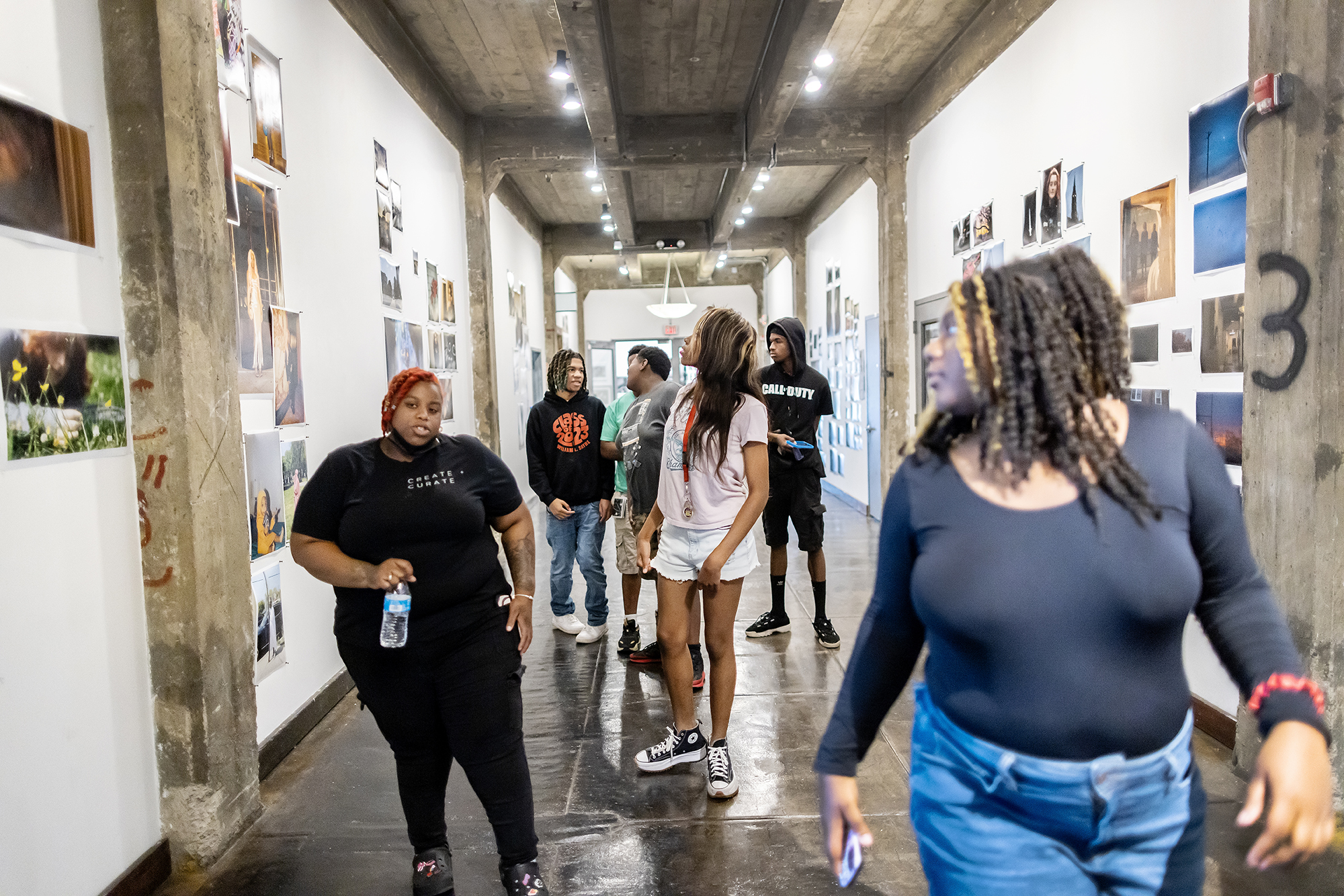 A group of students from Sayre with Latifah Wright in the hallway at TILT. Images from other teens are tacked on the drywall.