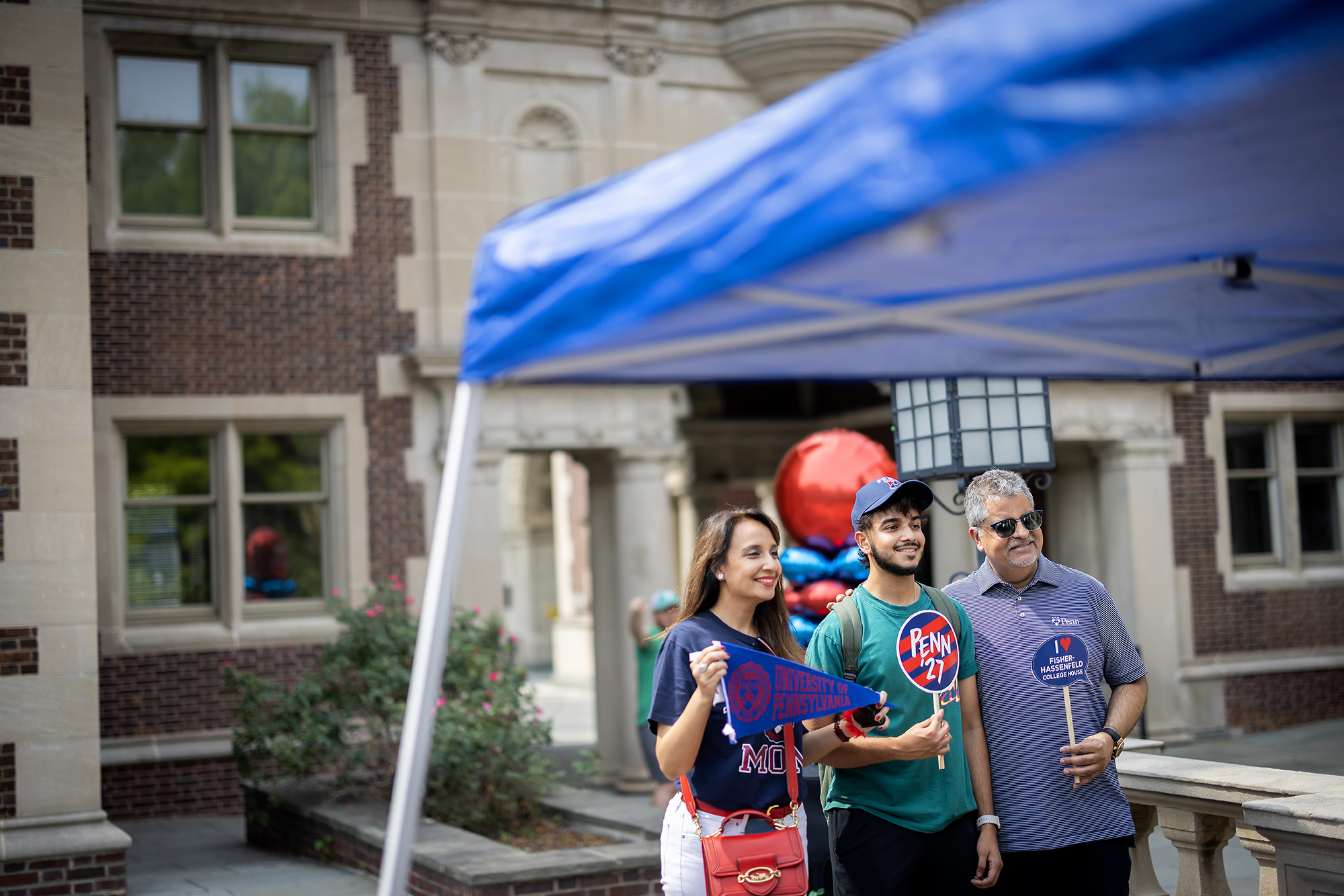 A new Penn student poses with their parents for a photo holding Penn banners.