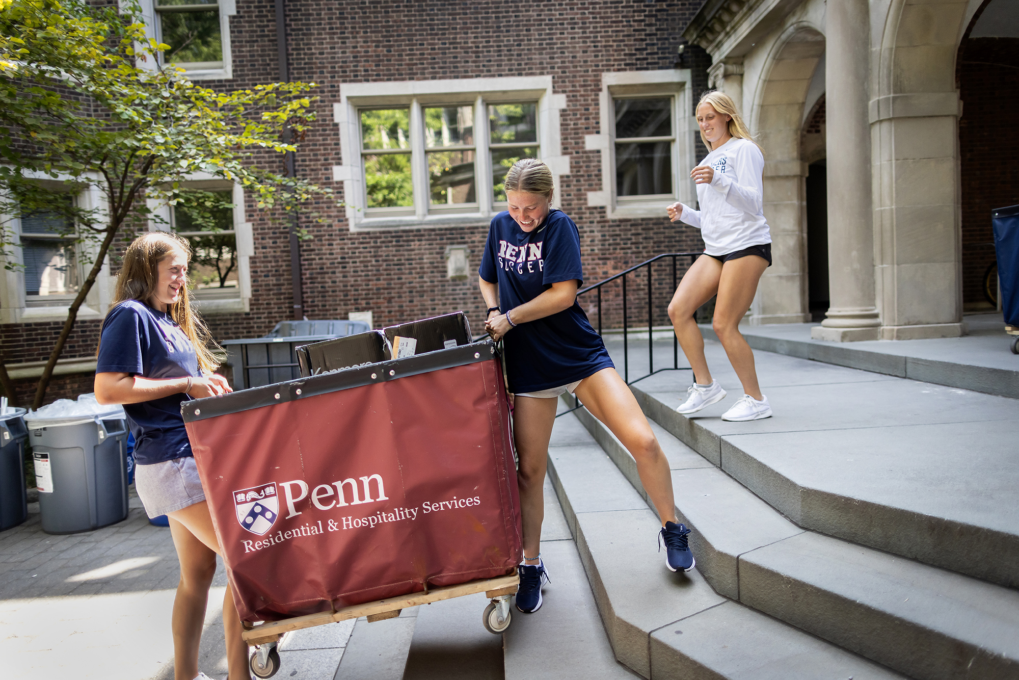 Three students move a large Move-In bin up stairs at a dorm on Penn’s campus.
