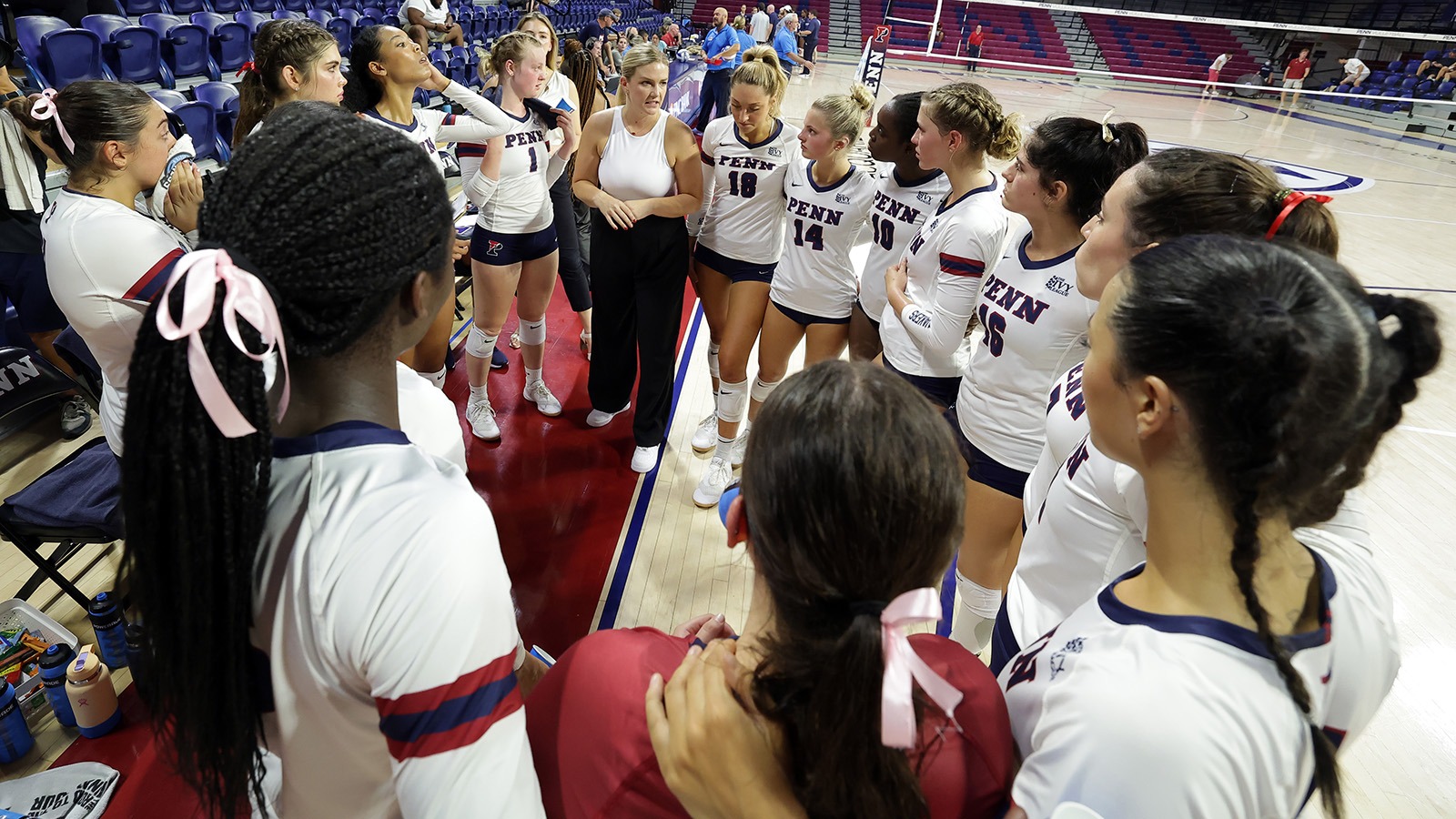 Members of the volleyball team stand in a huddle and listen to their coach.