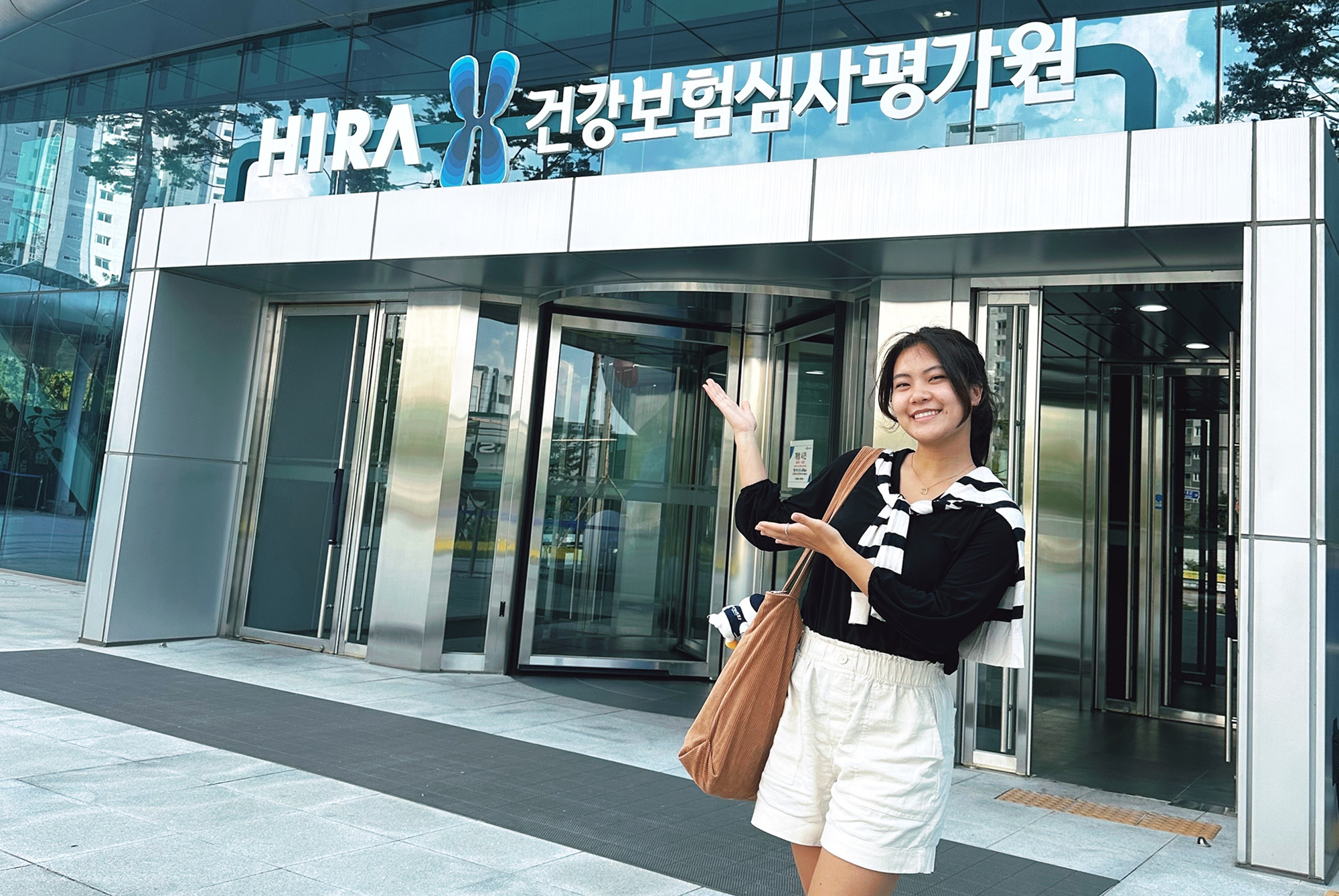 Penn undergrad Claire Jun gestures to the sign on the front of the building in Seoul, South Korea where she interned this summer.