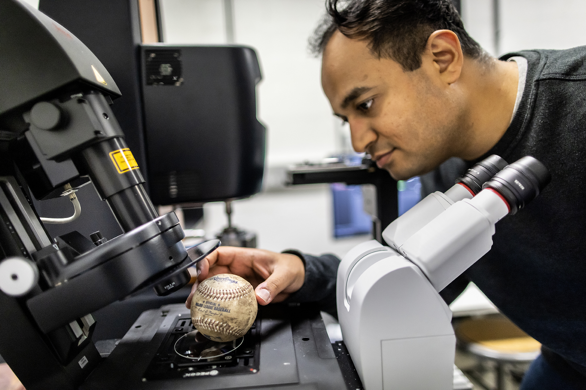 Shravan Pradeep places a baseball on microscopy slide.