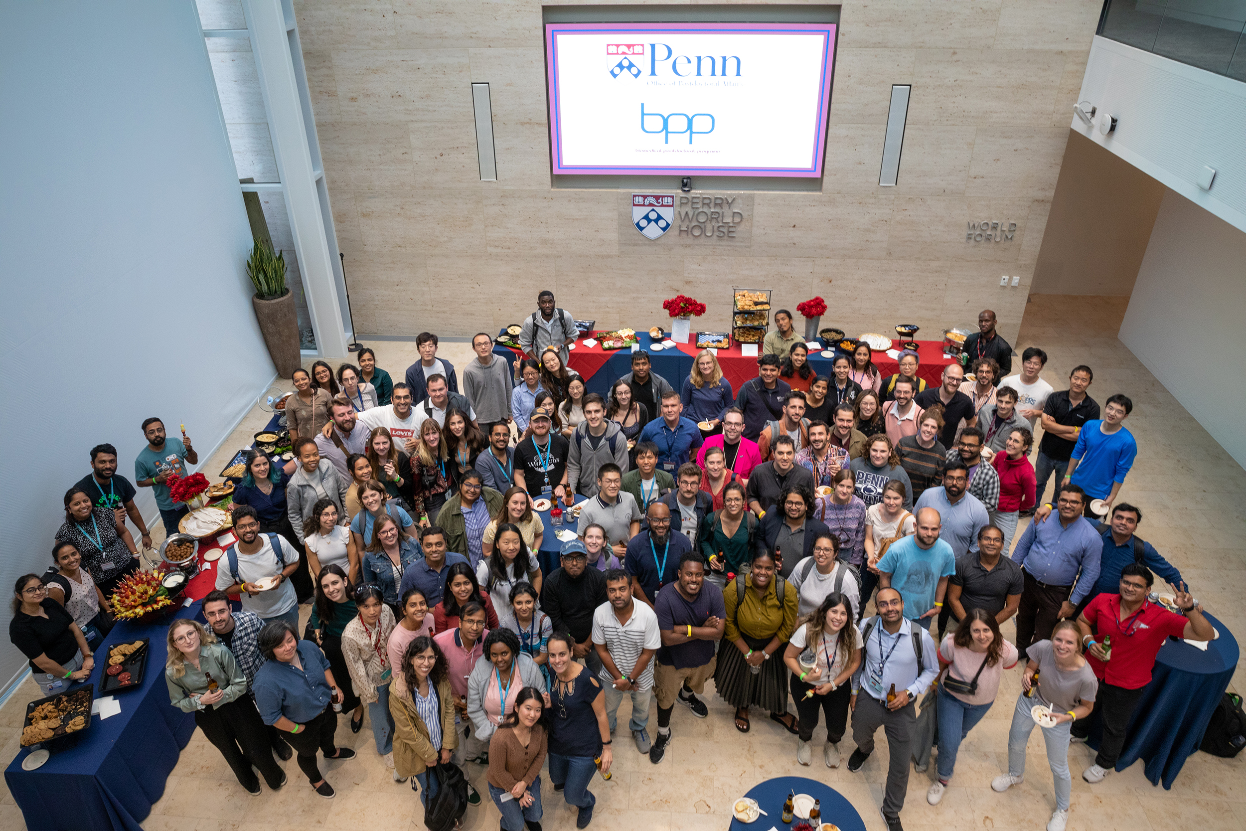 big group of postdocs pose for a photo, photo taken looking down. Screen in background reads: Penn and BPP
