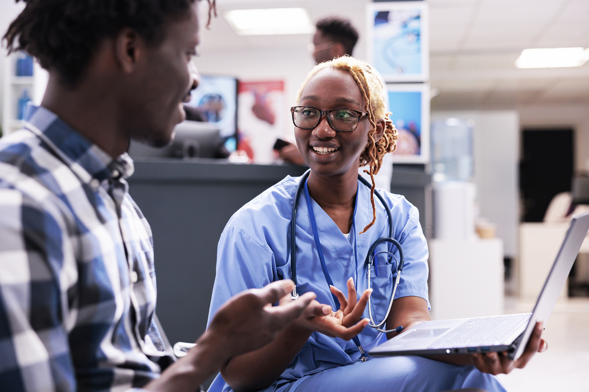 A doctor speaks with a patient while holding a laptop.