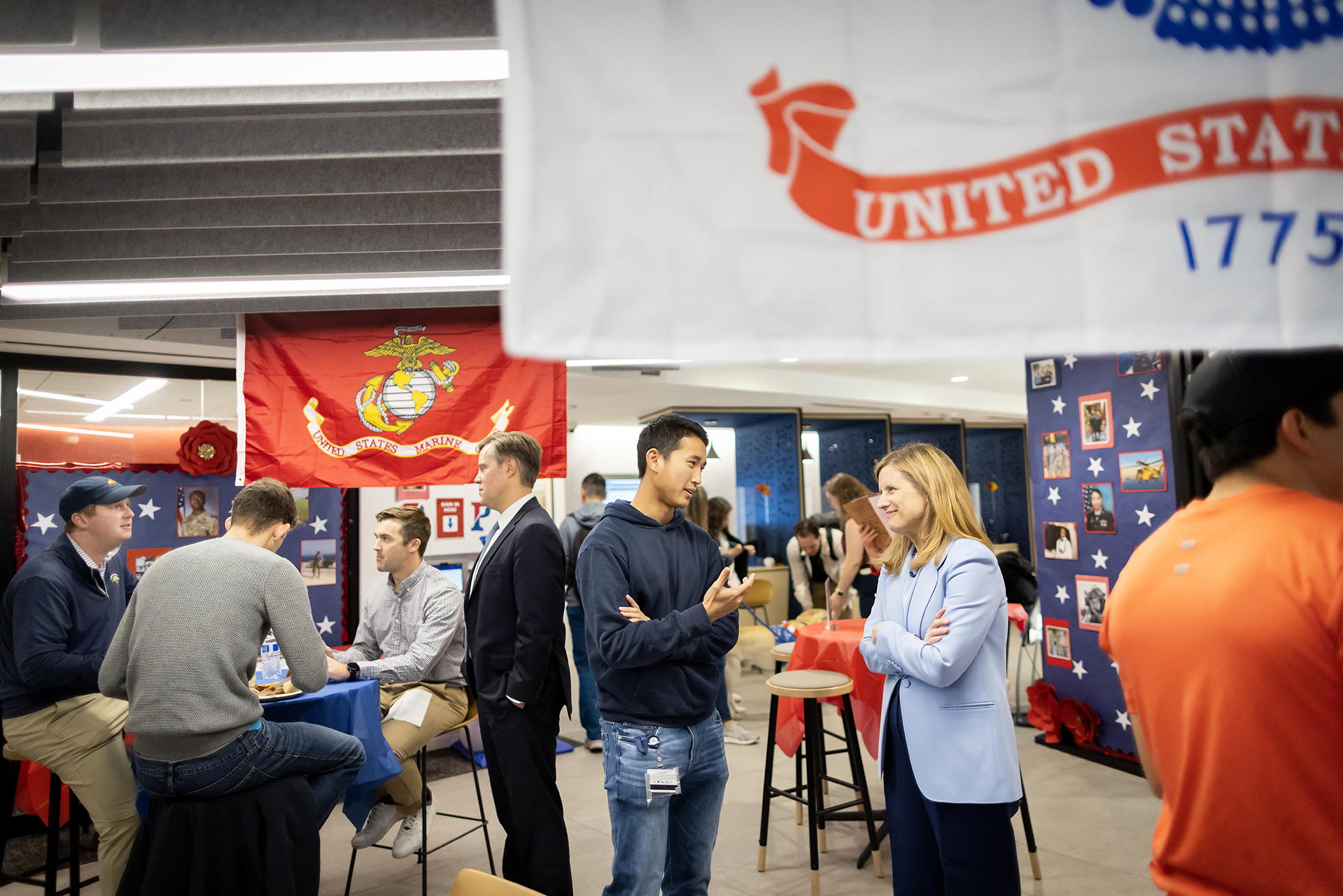 In a room decorated with armed services' flags, pictures of service members, and stars, President Liz Magill talks with Landon Le, a second-year student.