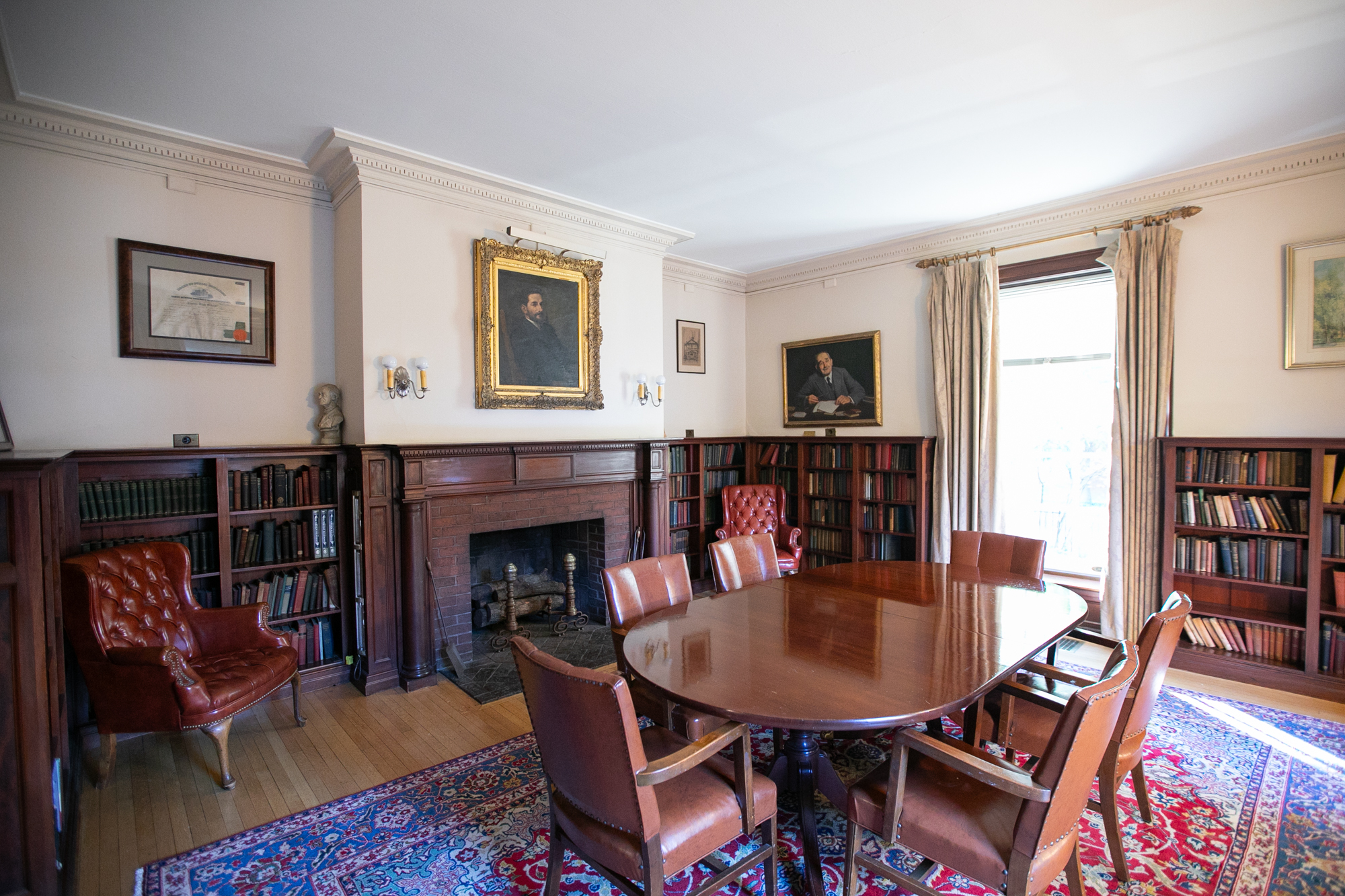 Interior of Fox-Fels Hall on Penn Campus, with wooden inlaid fireplace and low bookshelves, wooden dining table and oil paintings of people's portraits on the walls.