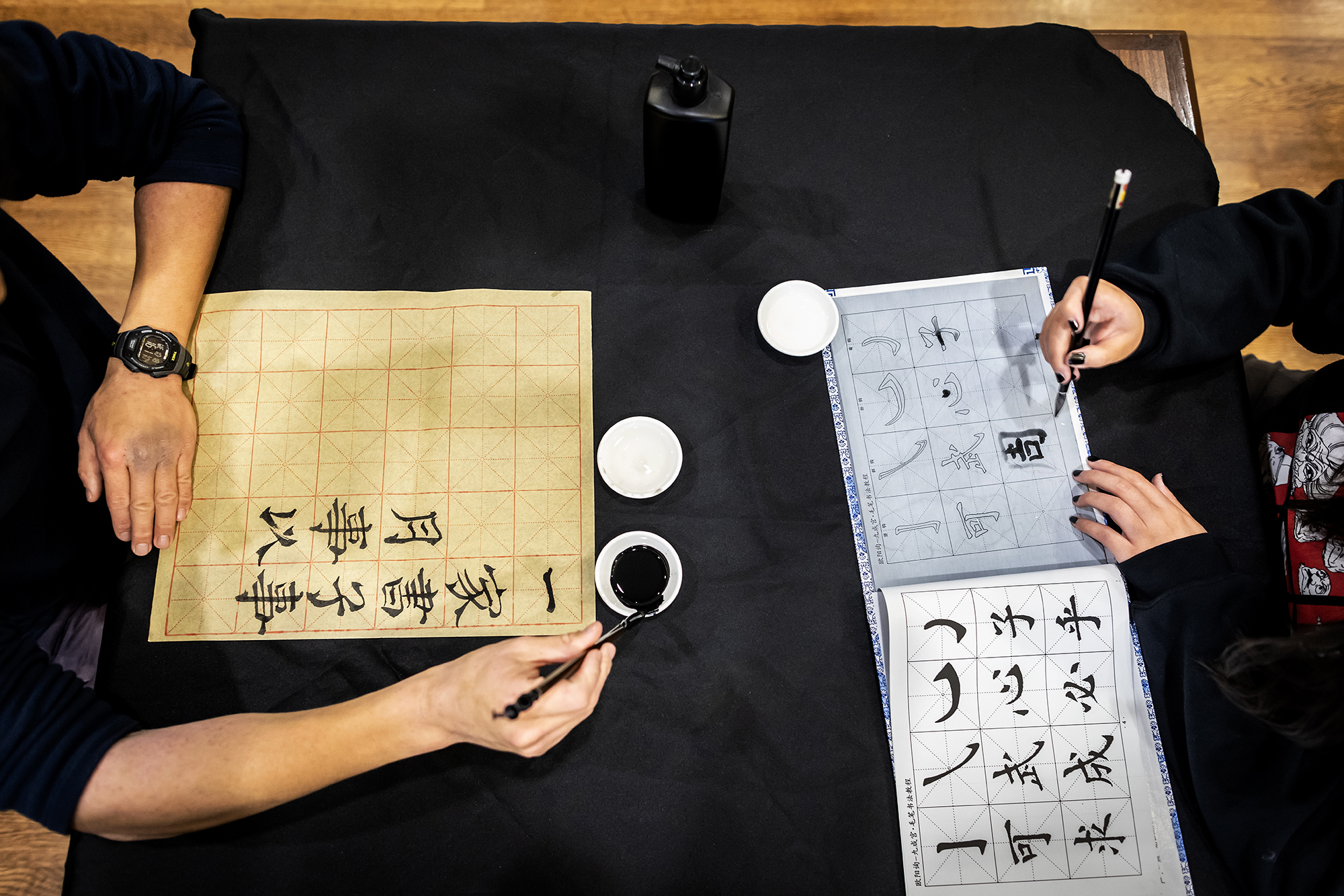 Hands holding calligraphy brush as they paint. 