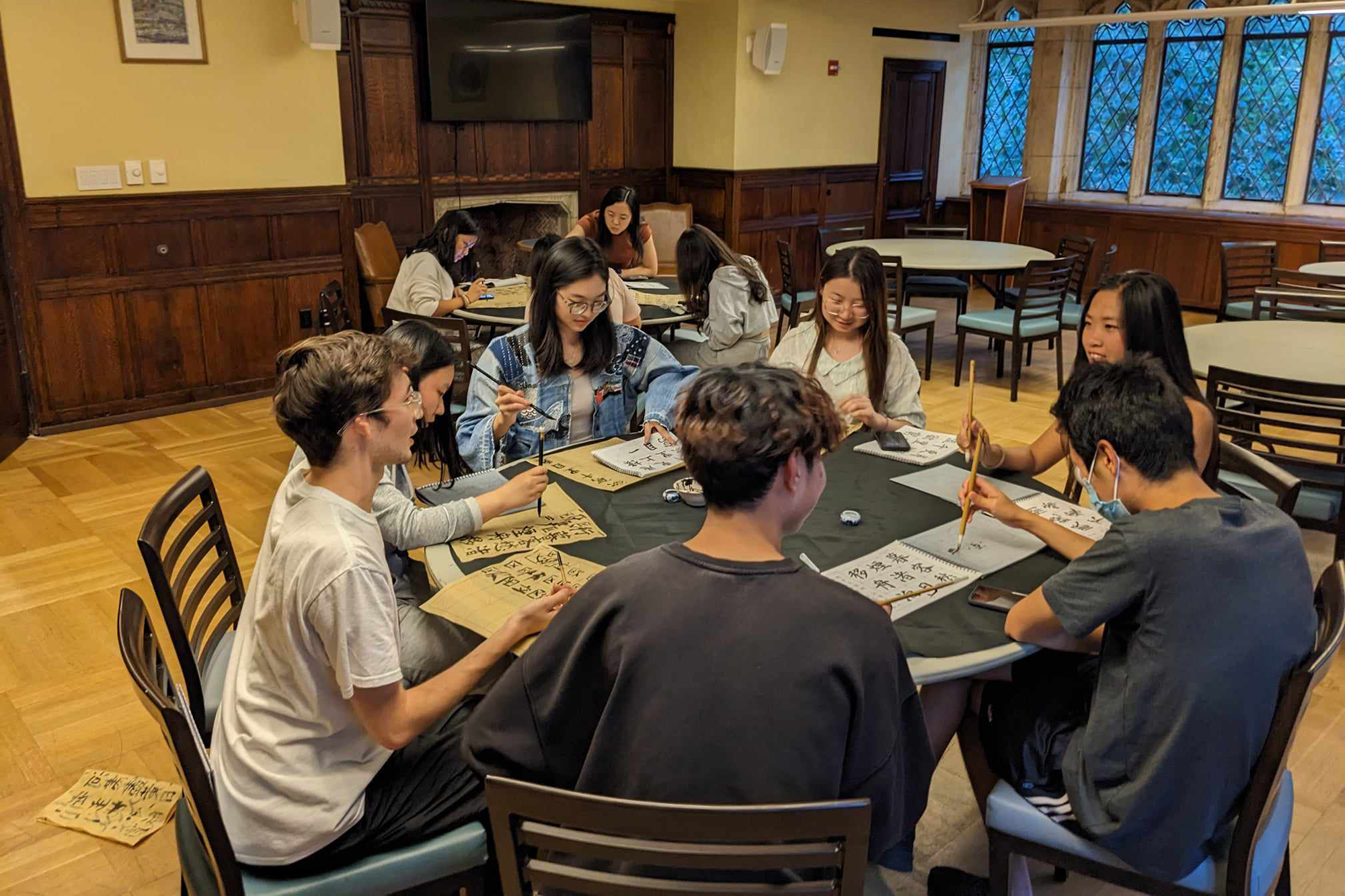 Students painting with Chinese calligraphy brushes while gathered around a table. 