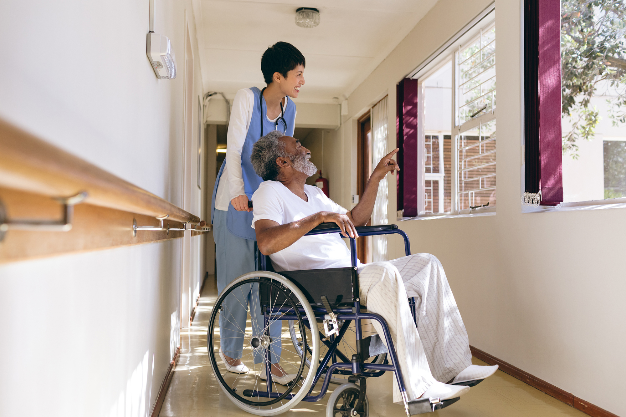 A nursing home worker pushing a patient in a wheelchair.