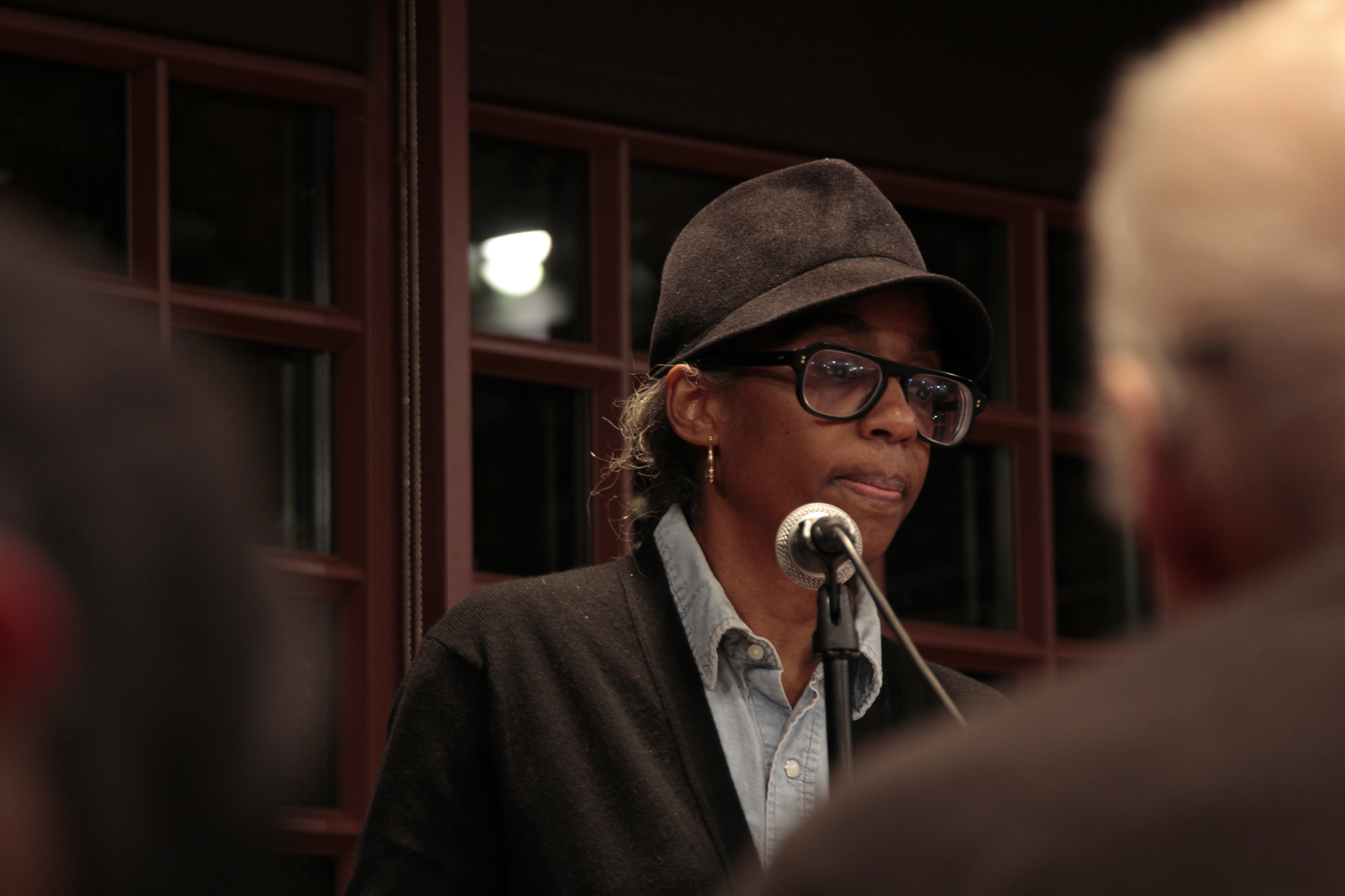Simone White wearing a hat and glasses reading at a microphone.