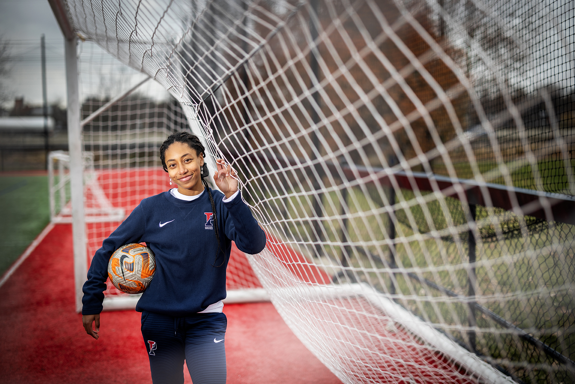 Ginger Fontenot, wearing a Penn sweatsuit, holds a soccer ball inside a goal at Penn Park.