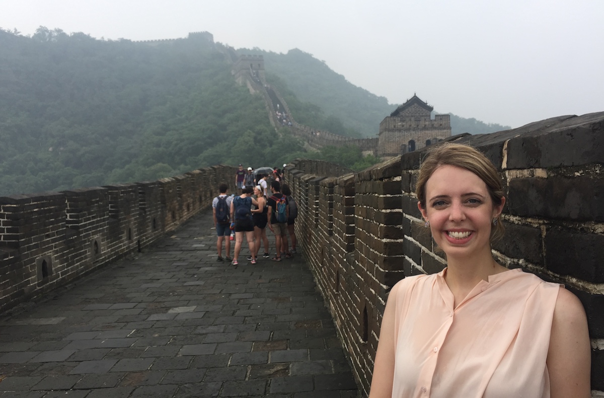 Rachel Hulvey stands on the Great Wall of China, with a hazy mountain in the background.