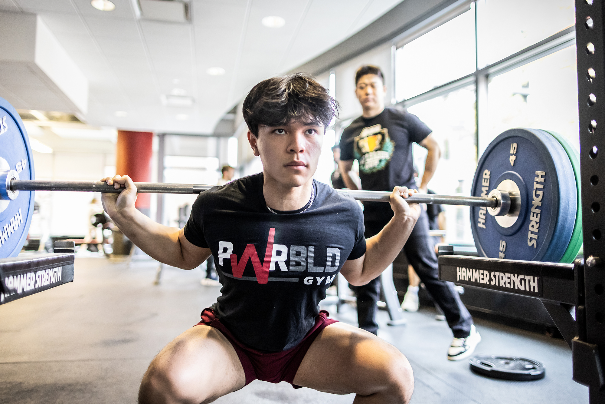 A student performs a barbell squat, which works your glutes, quads, and other leg muscles. 