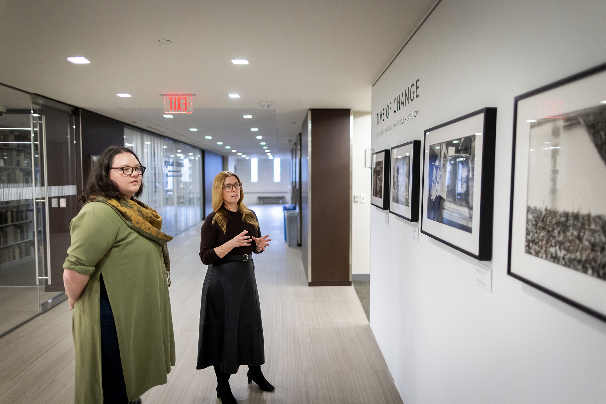 Brittany Merriam and Lynn Dolby standing in hallway in Libraries looking at photographs on wall