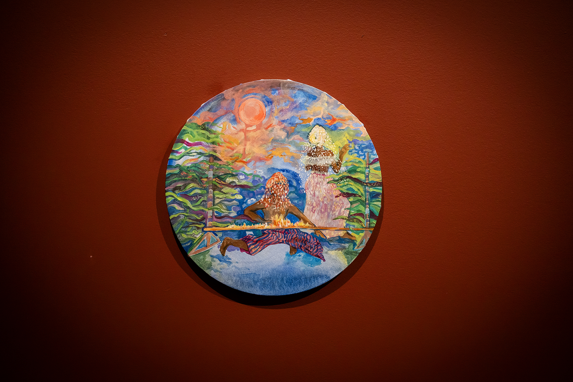 Round painting with two figures and a sun casting on them in the sky.