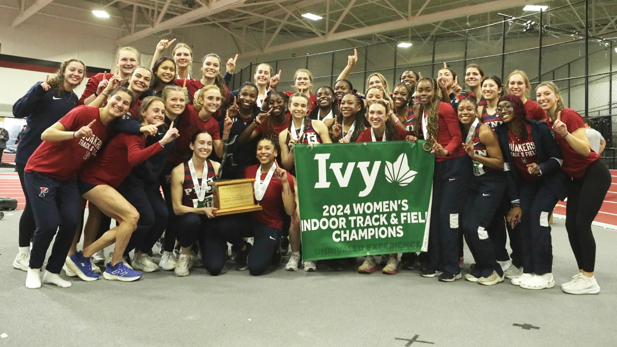 Members of the women's track and field team pose with the Indoor Ivy Heps championship banner after winning the competition at Harvard.