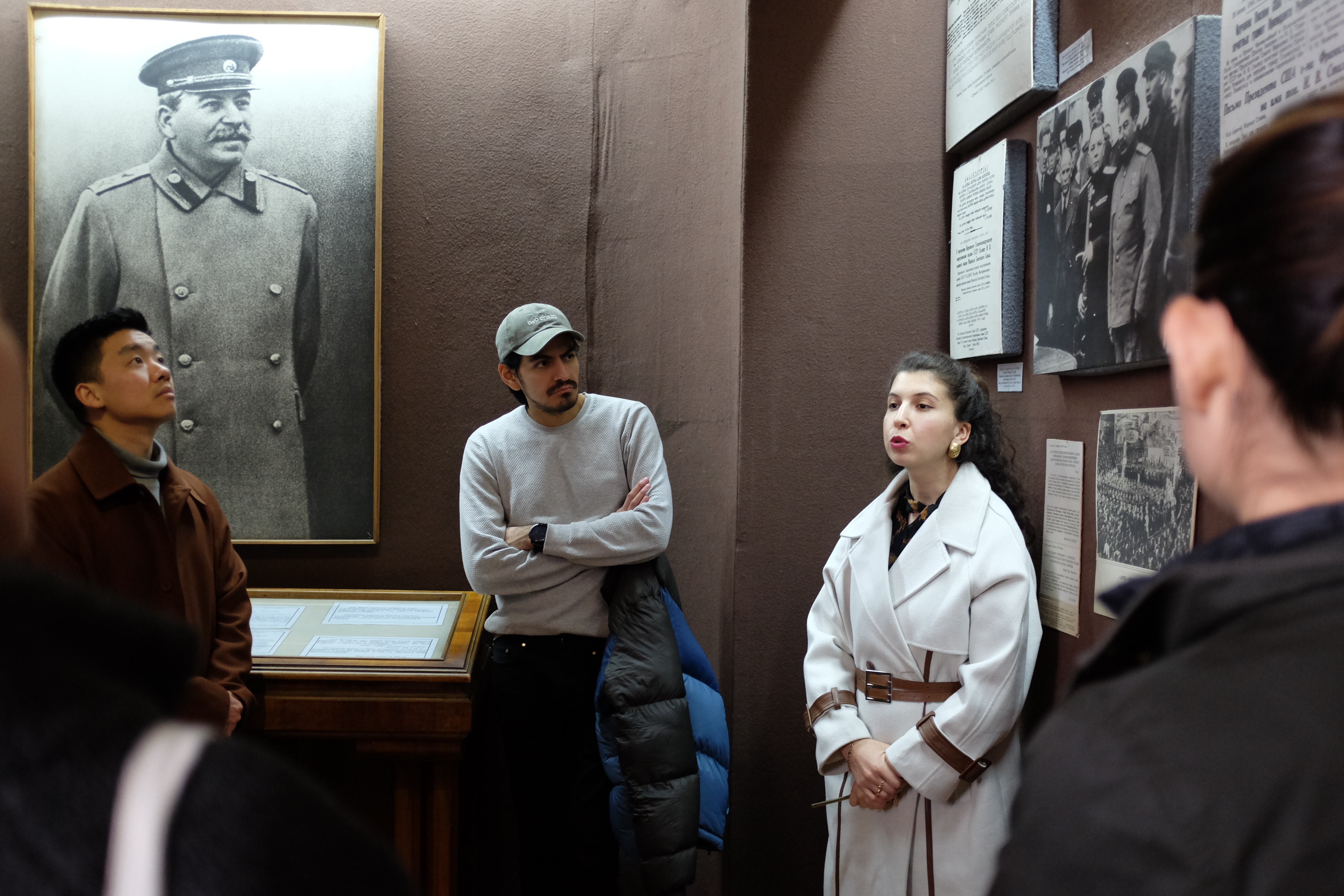 People gathered in a museum with a portrait of Joseph Stalin in the background.