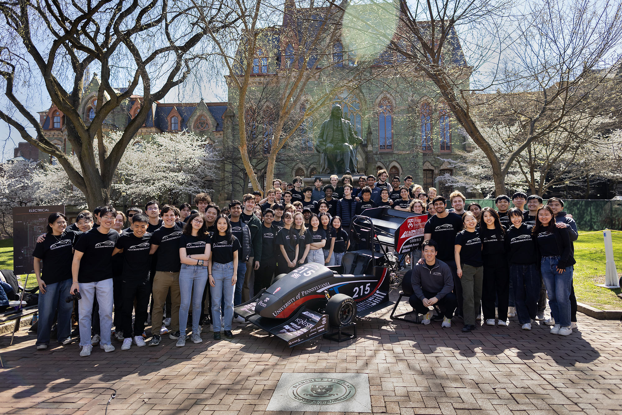 A large group A large group of students stands around an electric formula racing car.