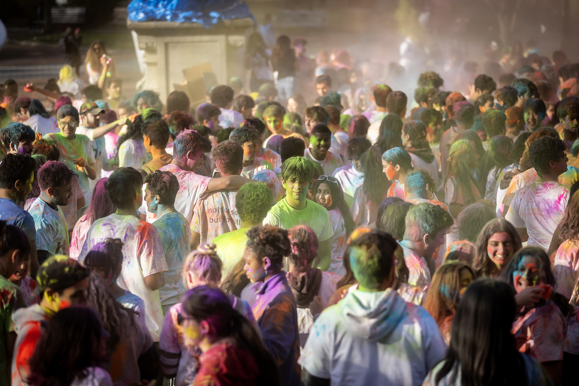 A crowd of Penn students covered in colored powder celebrating Holi on College Green.