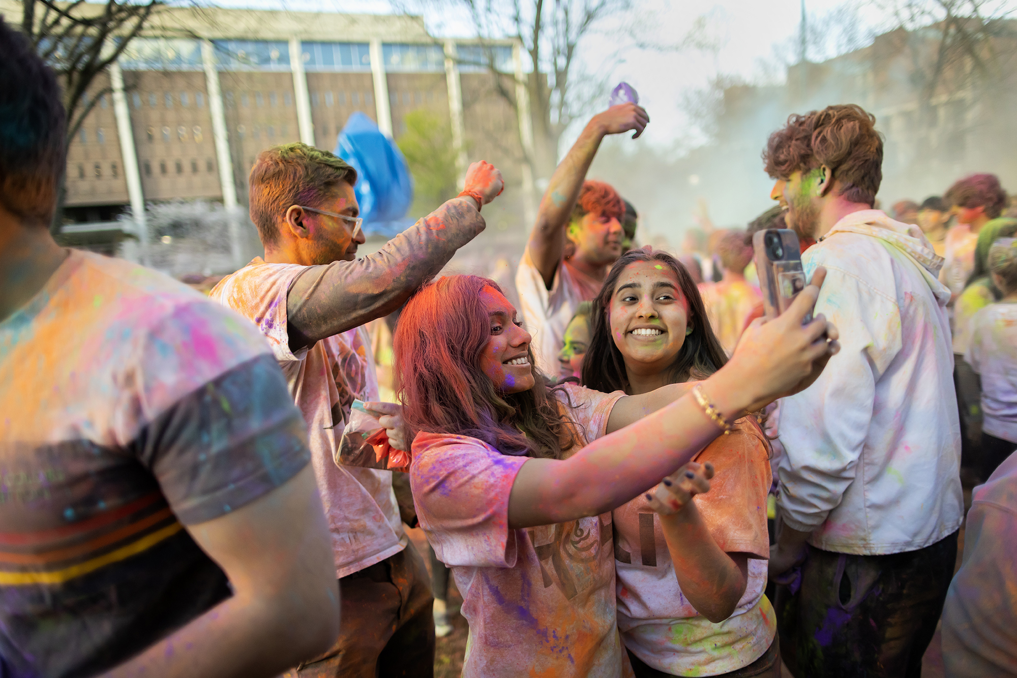 Students pose for a selfie while covered in powder while celebrating Holi on College Green.