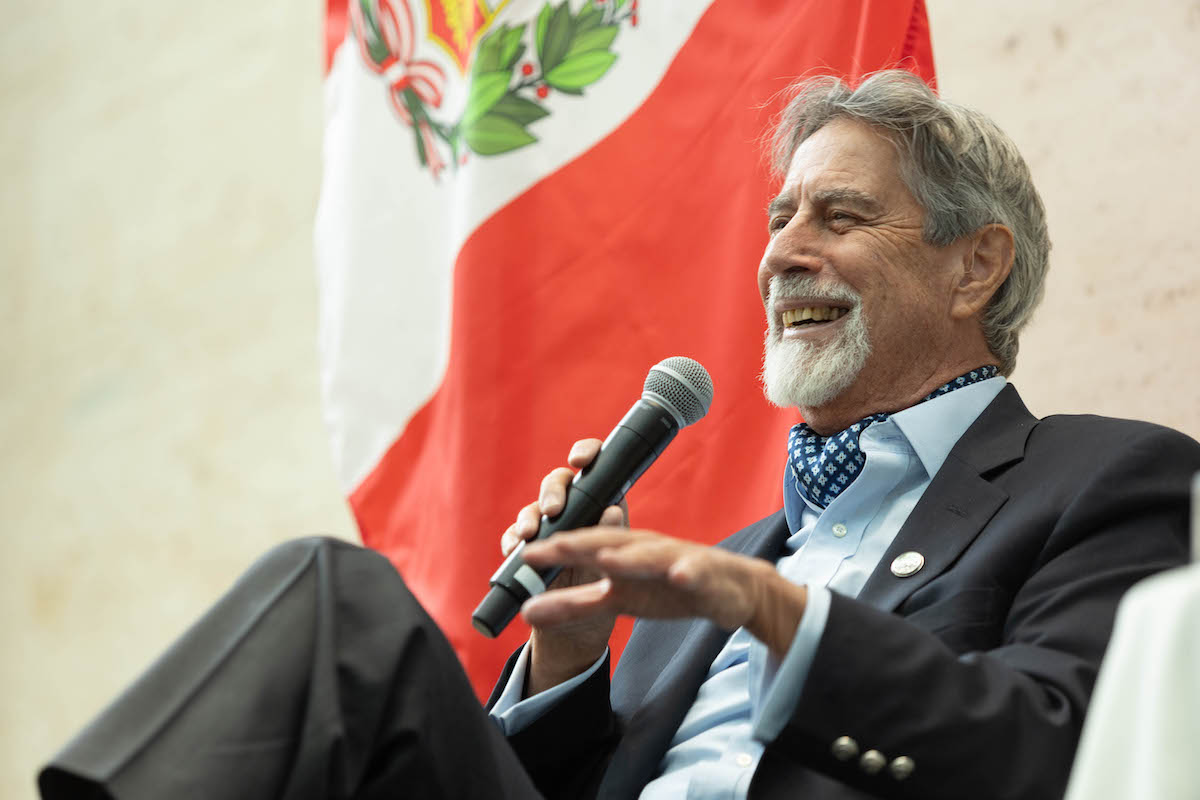 Former Peruvian President Sagasti Smiles as he is seated in front of the Peruvian flag, speaking into a microphone.