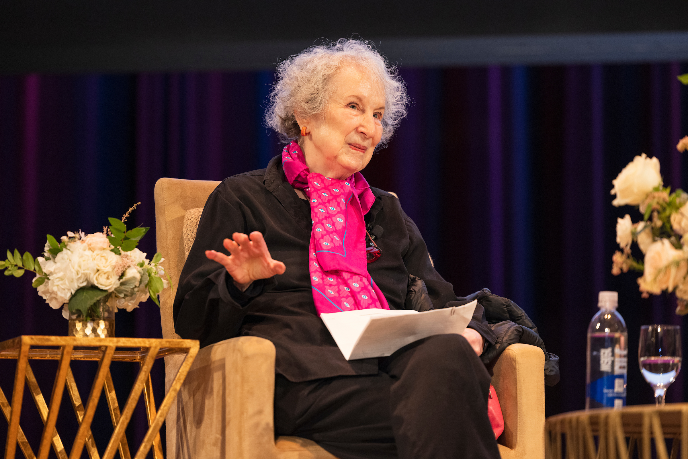 Margaret Atwood sitting in a chair gesturing with her right hand and holding a paper in her left hand on her lap