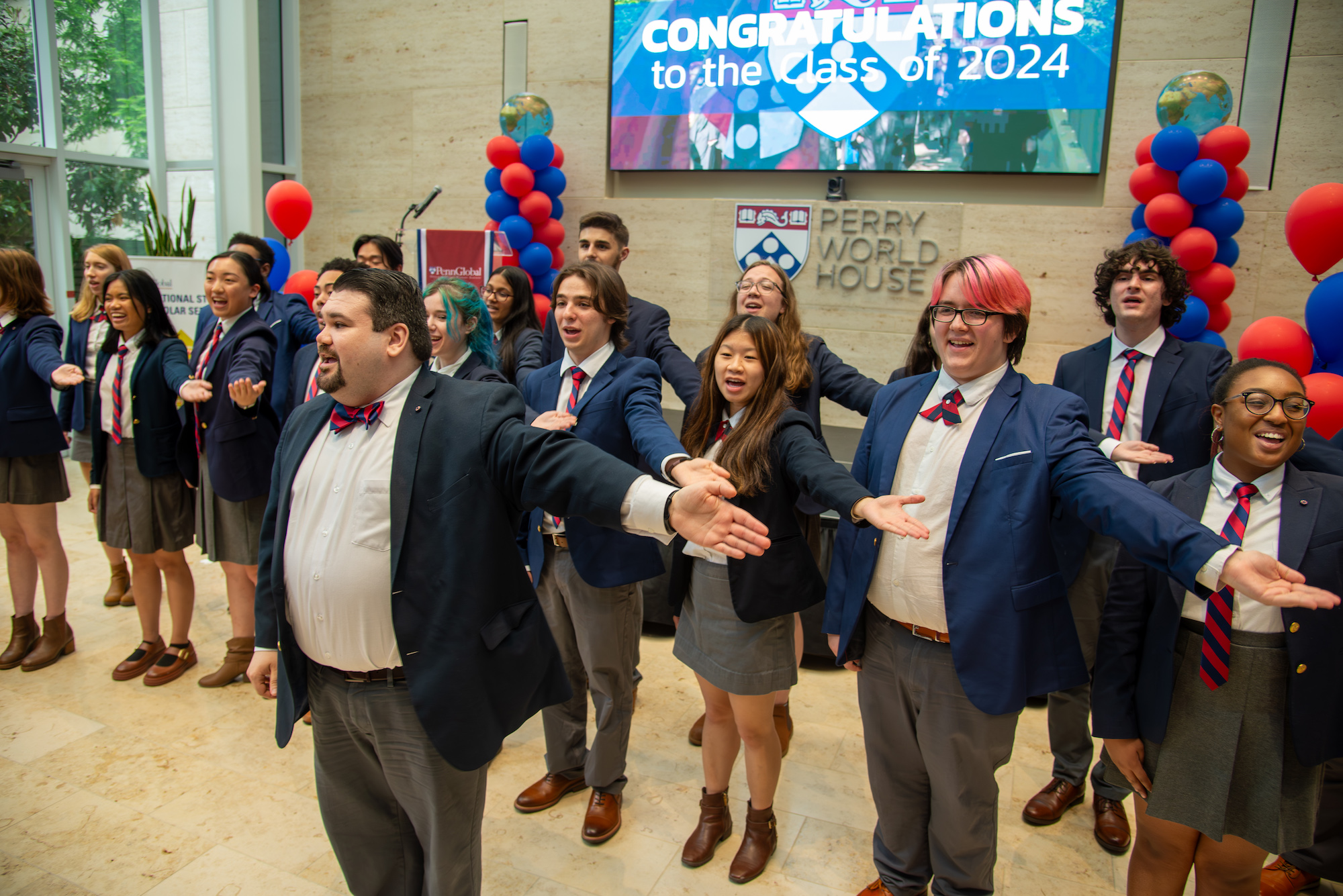 Penn Glee club performs at Perry World House, with towers of red and blue balloons behind them.