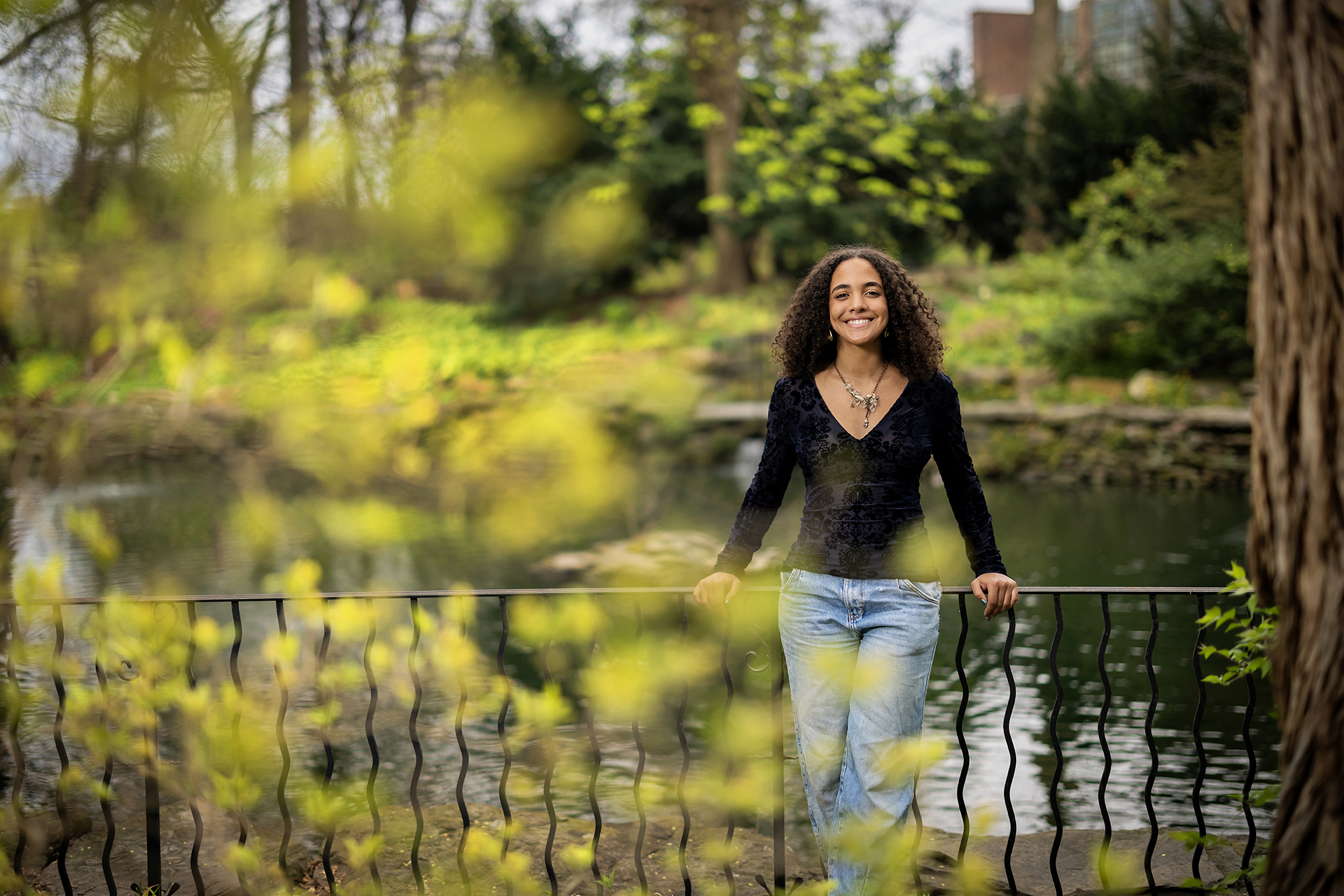 Mya Gordon leans against a fence at the biopond, with spring foliage in the foreground