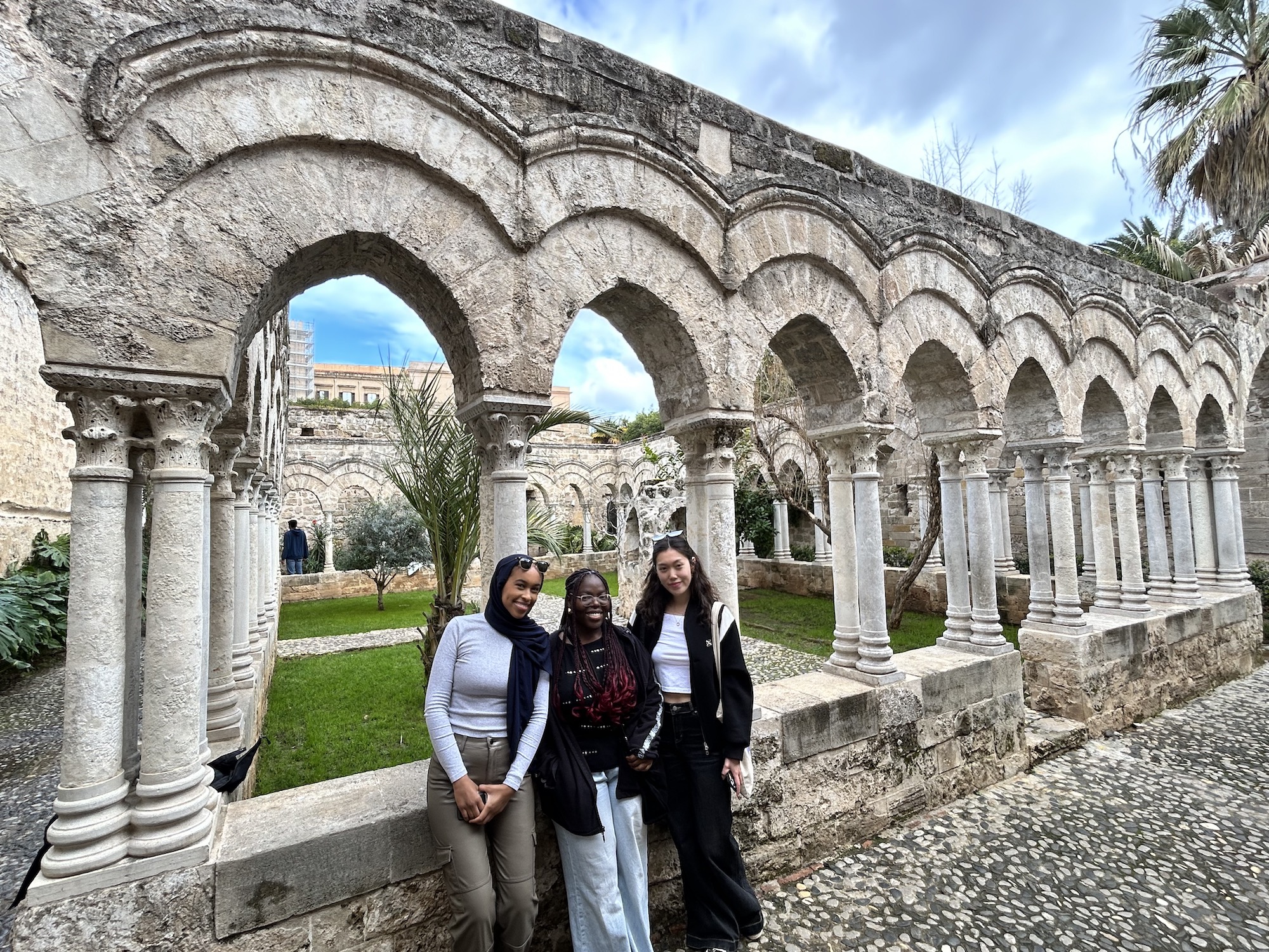 Three students pose in front of arches at the cloister of San Giovanni degli Eremiti, a historic monastery in Palermo.