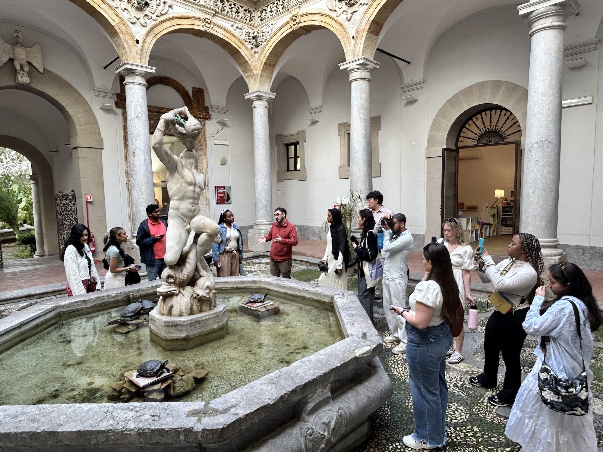 Students listen to Professor Domenic Vitiello in front of a fountain in a courtyard inside the Antonio Salinas Regional Archaeological Museum in Palermo. 