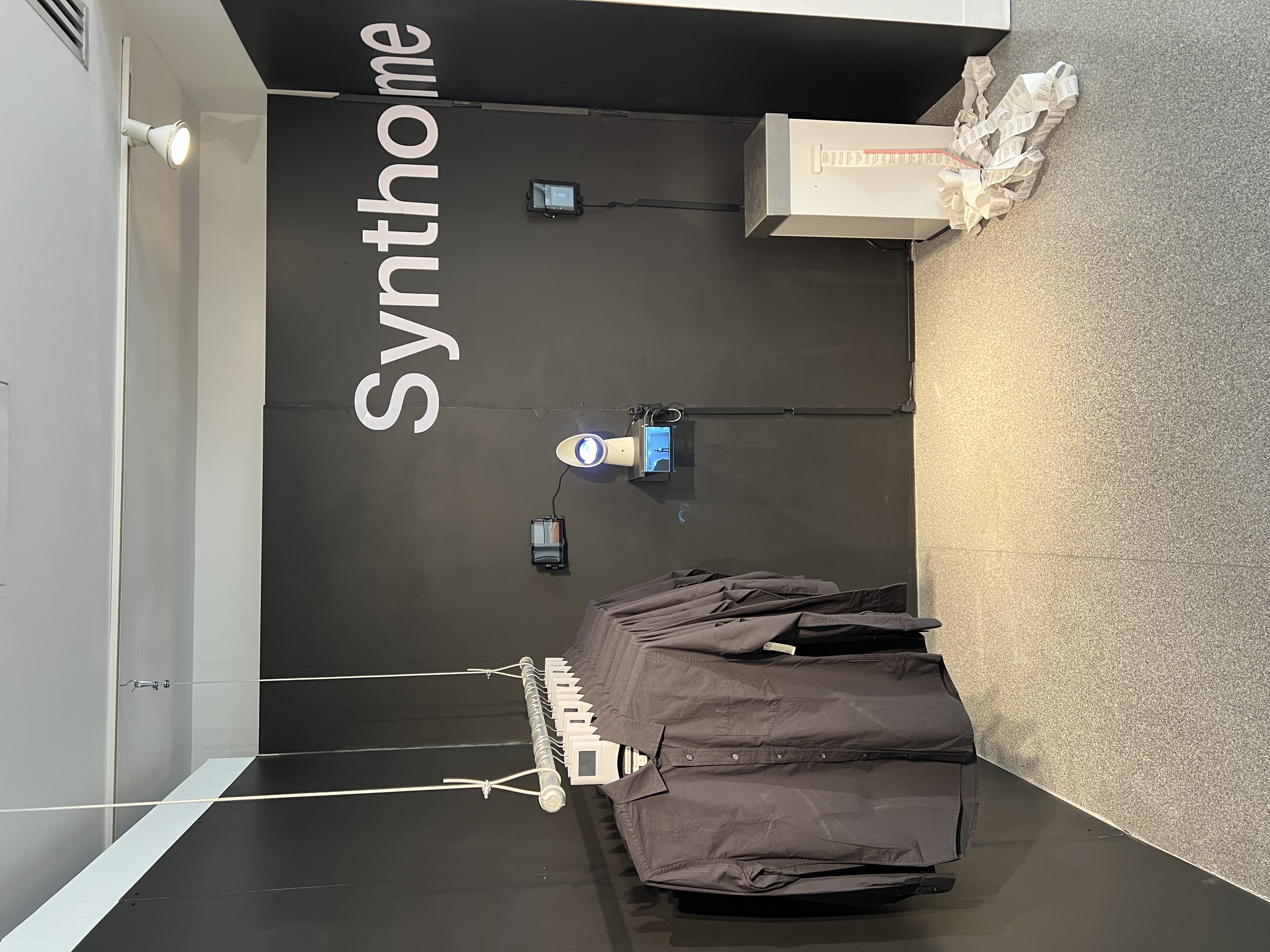 Exhibit that reads 'Synthome' and has T-shirts on a coat hanger and a trash can.