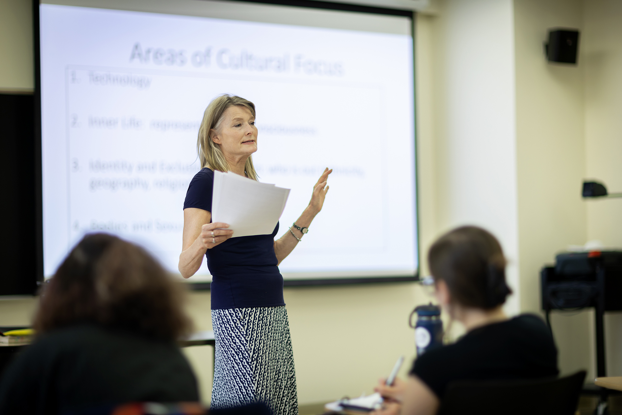 Jennifer Egan in front of class speaking with one hand up and the other holding papers