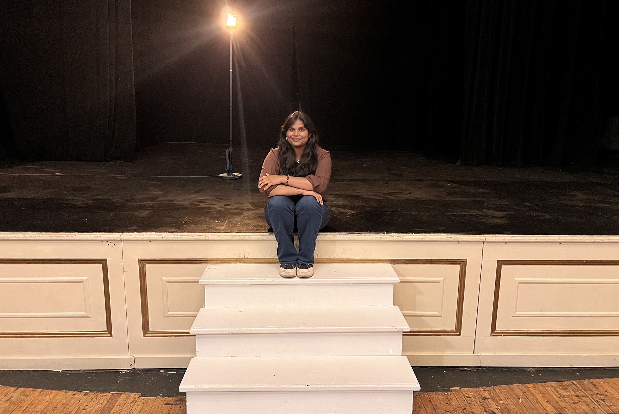 A Penn student doing an 1812 internship seated on a theater stage.