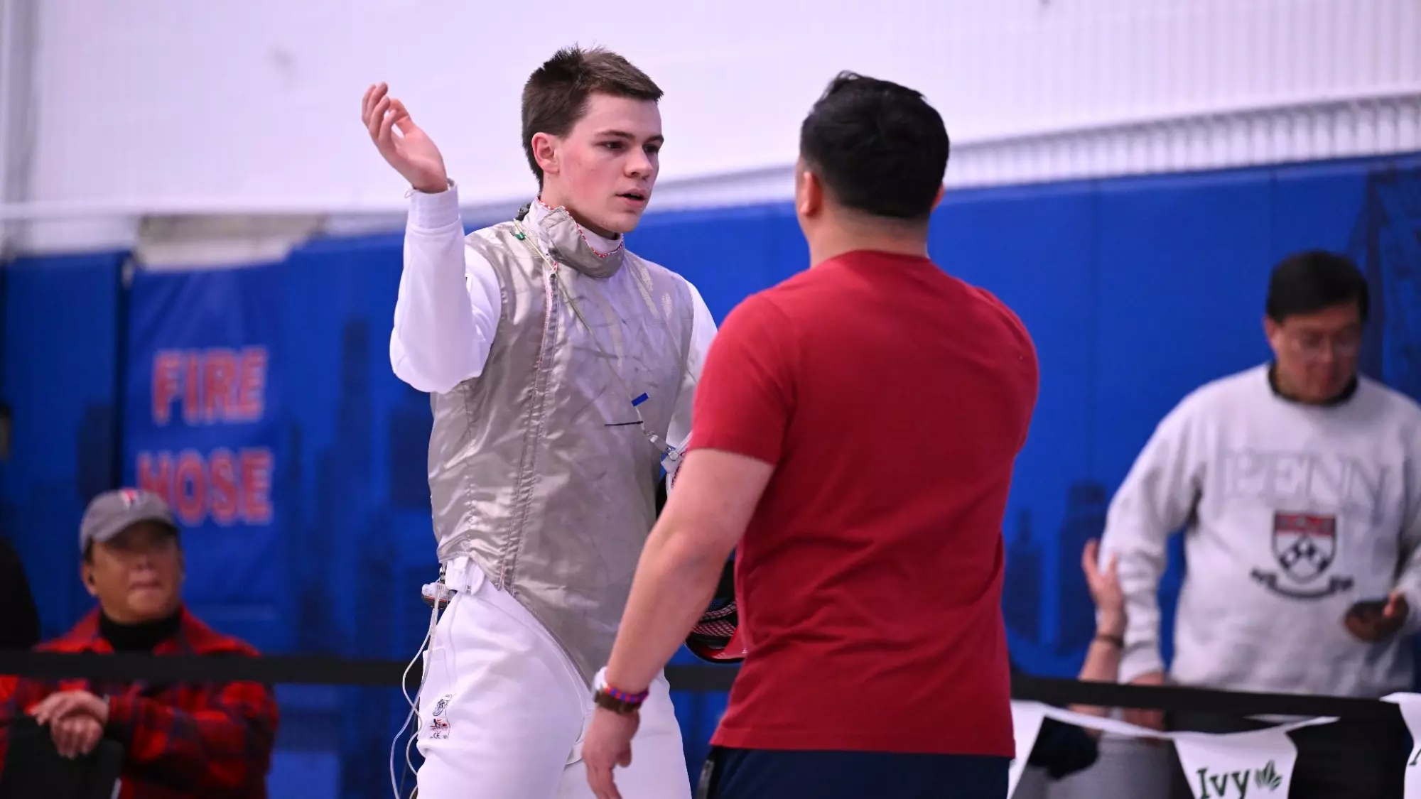 Blake Broszus, wearing his Penn fencing gear, chats with a coach