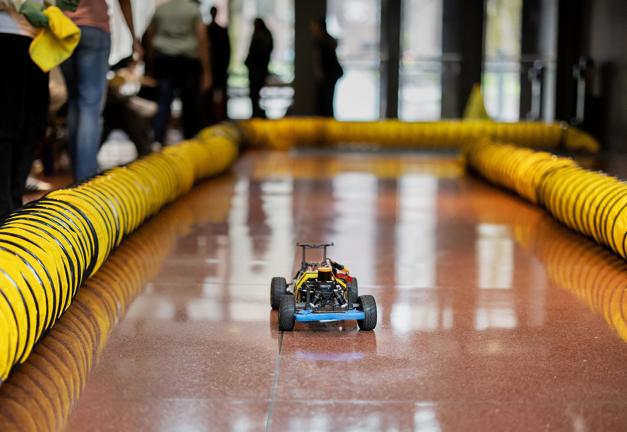 A small racecar in a makeshift track in Penn Engineering with student spectators.