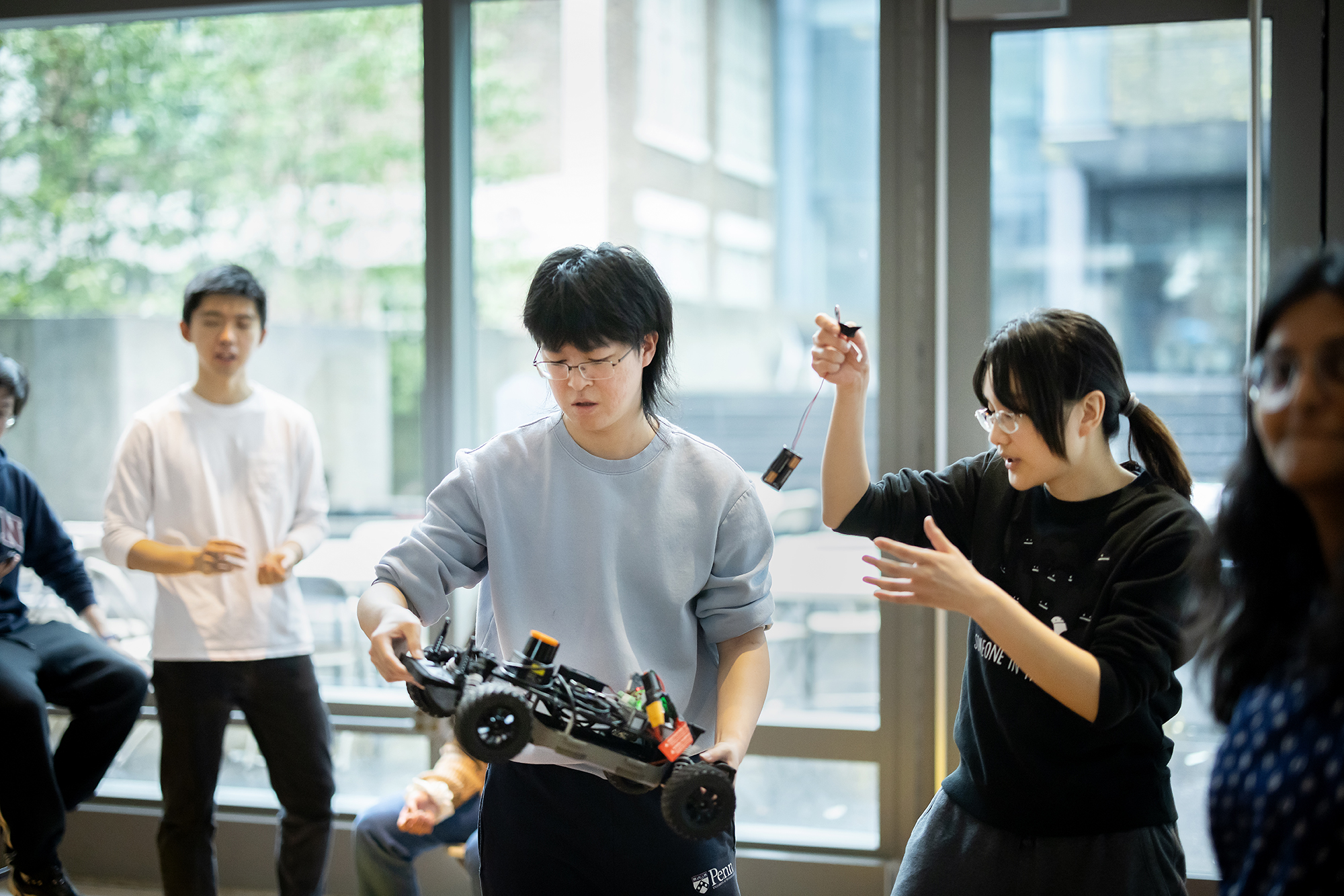 Penn students troubleshoot the building of a model race car that one student is holding.