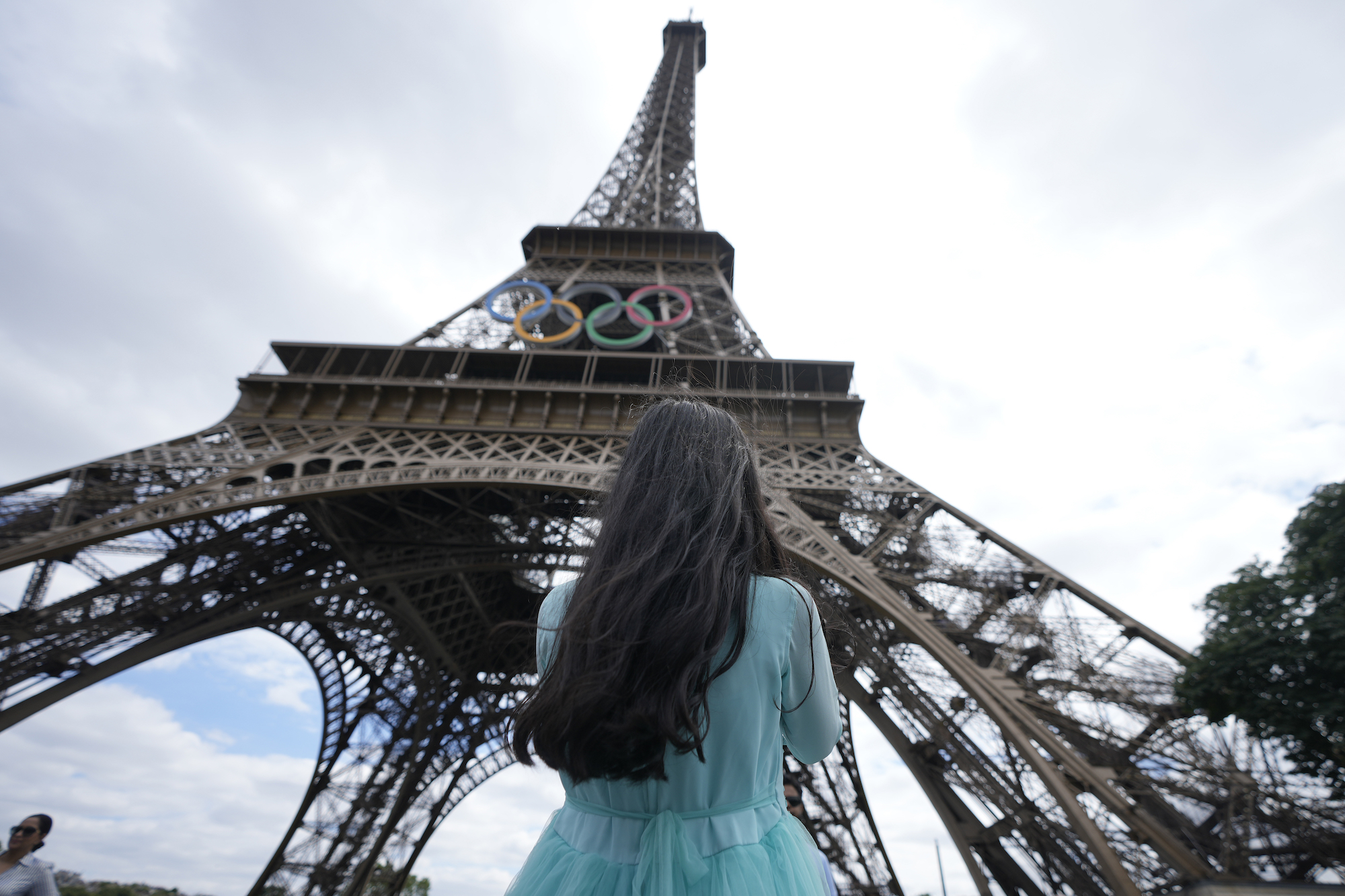 Tourist stands in front of Eiffel Tower in Paris, with Olympic rings on the exterior.
