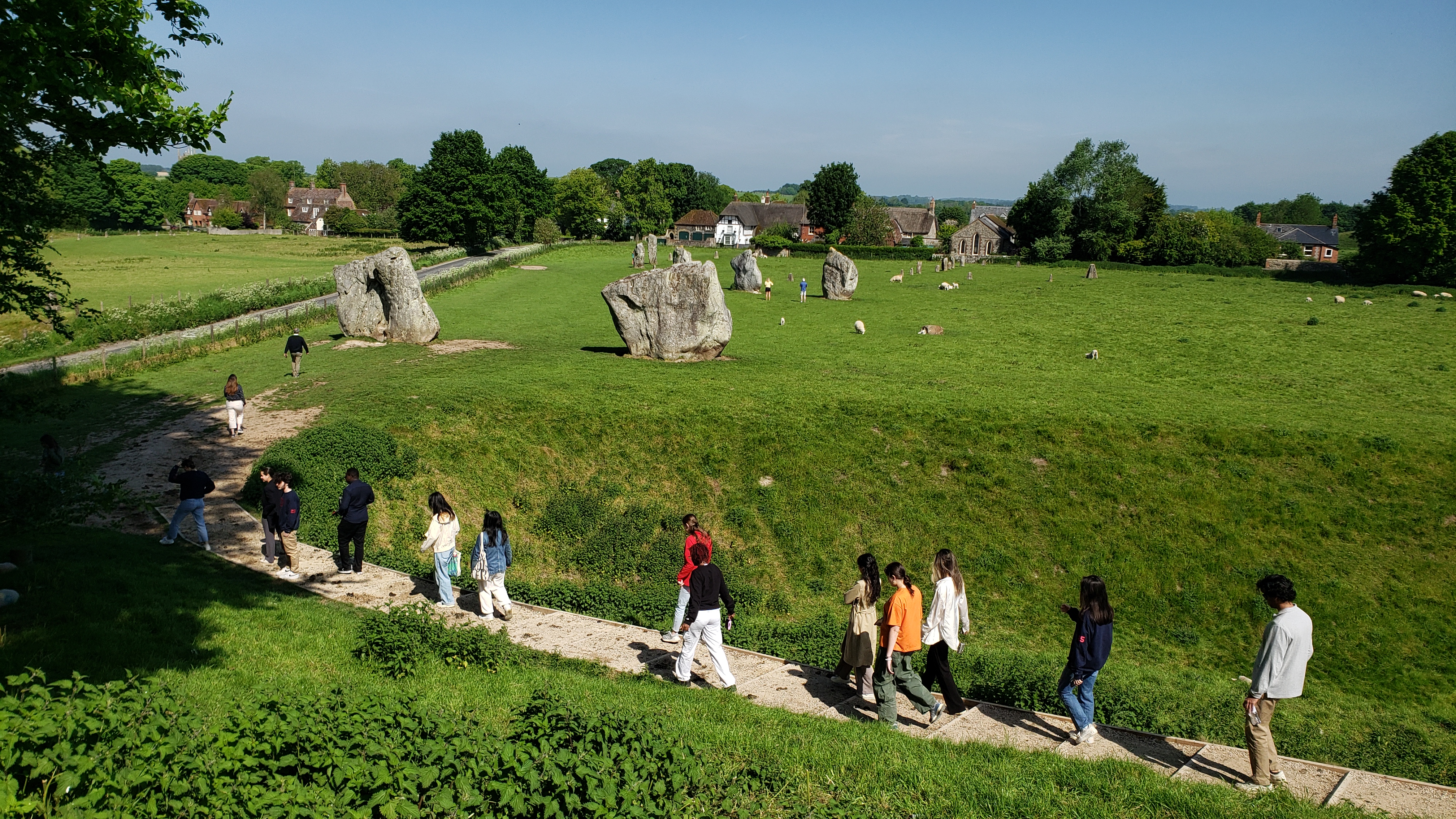 Students walk up a curved dirt path to a large field of stones. 