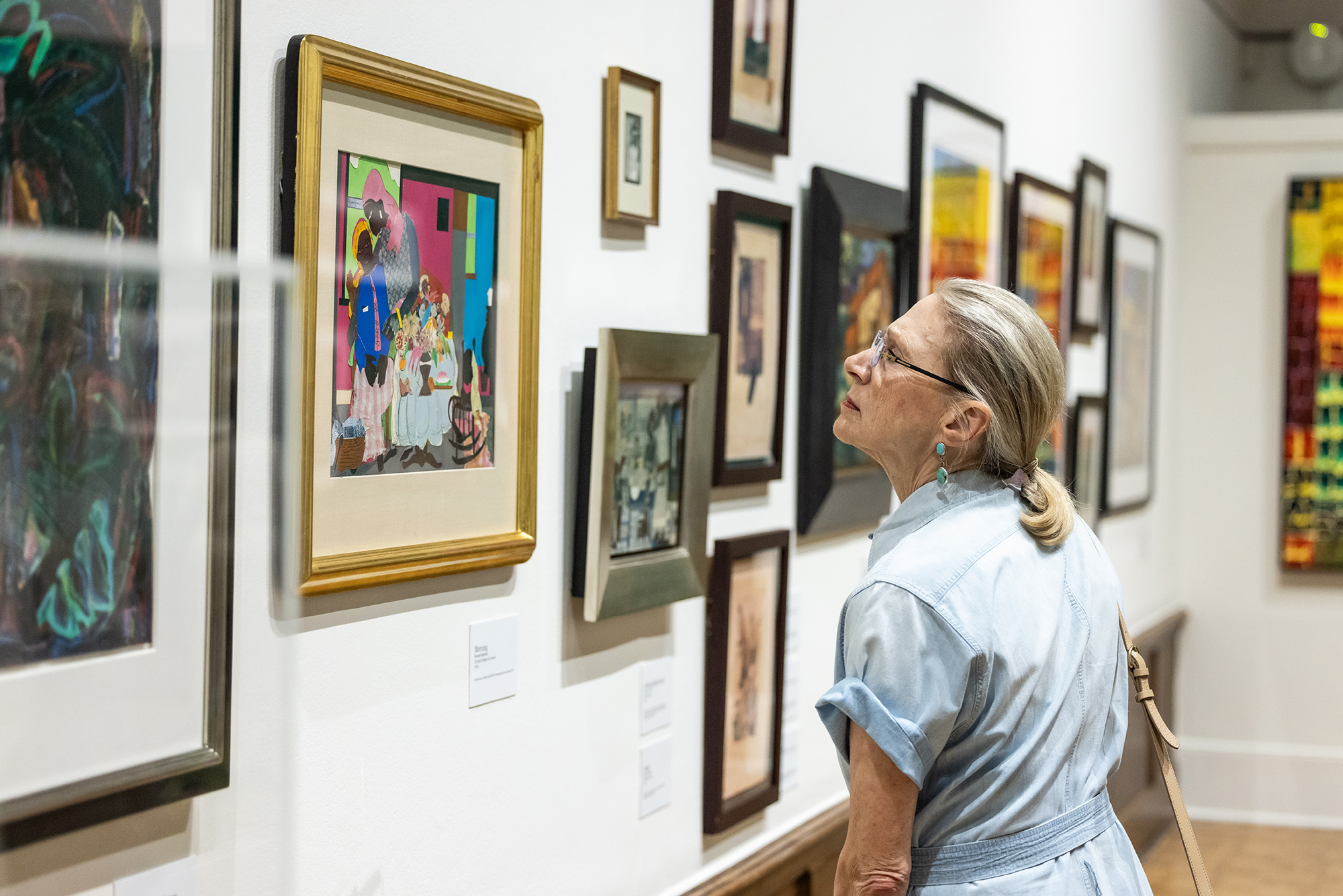 A person looking closely at a David Driskell painting on the wall at the Arthur Ross Gallery