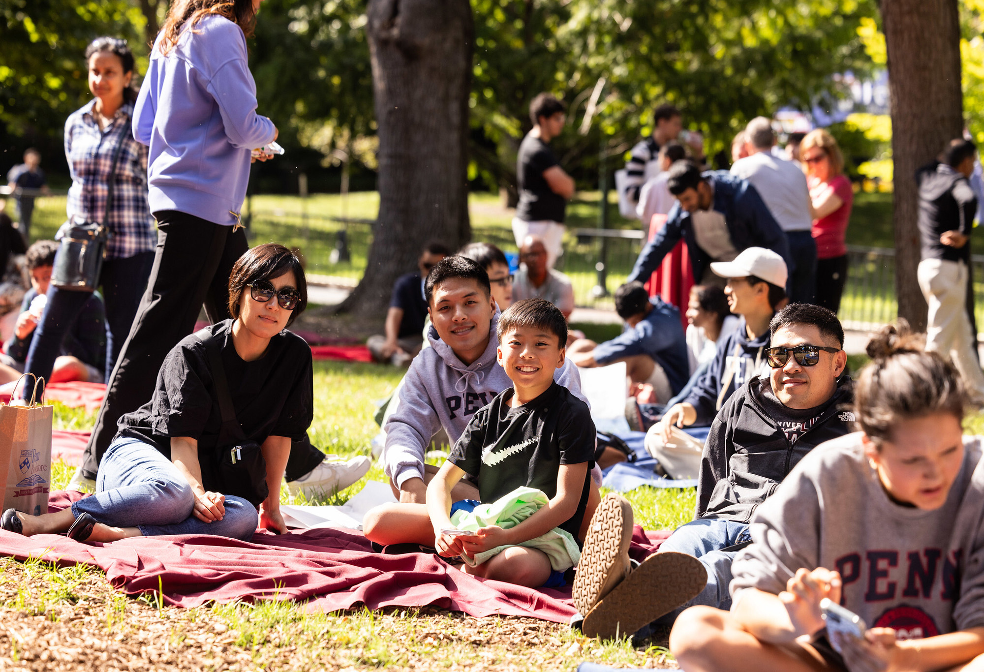 Penn friends and families sit on red blankets on College Green.