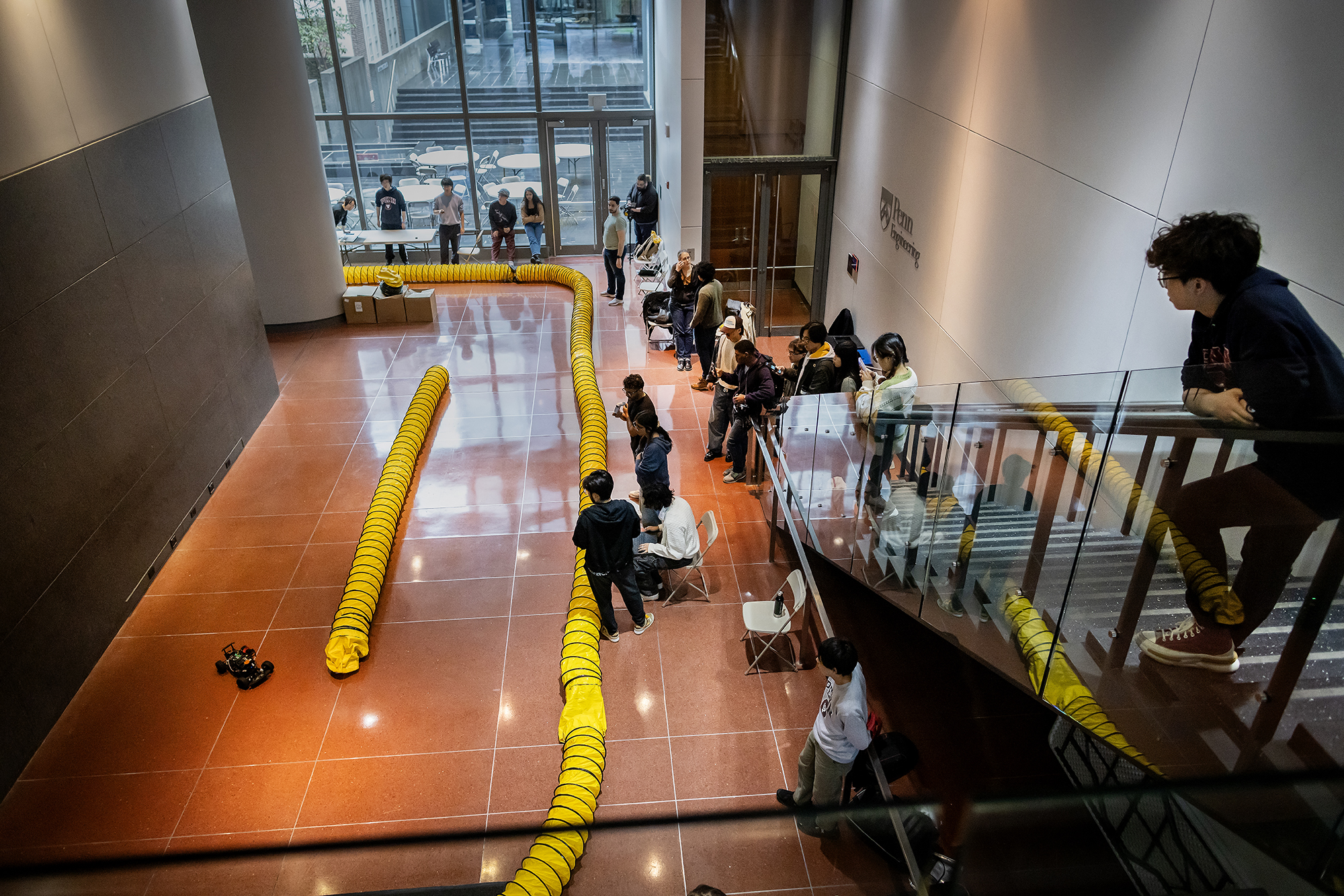 A small racecar in a makeshift track in Penn Engineering with student spectators.