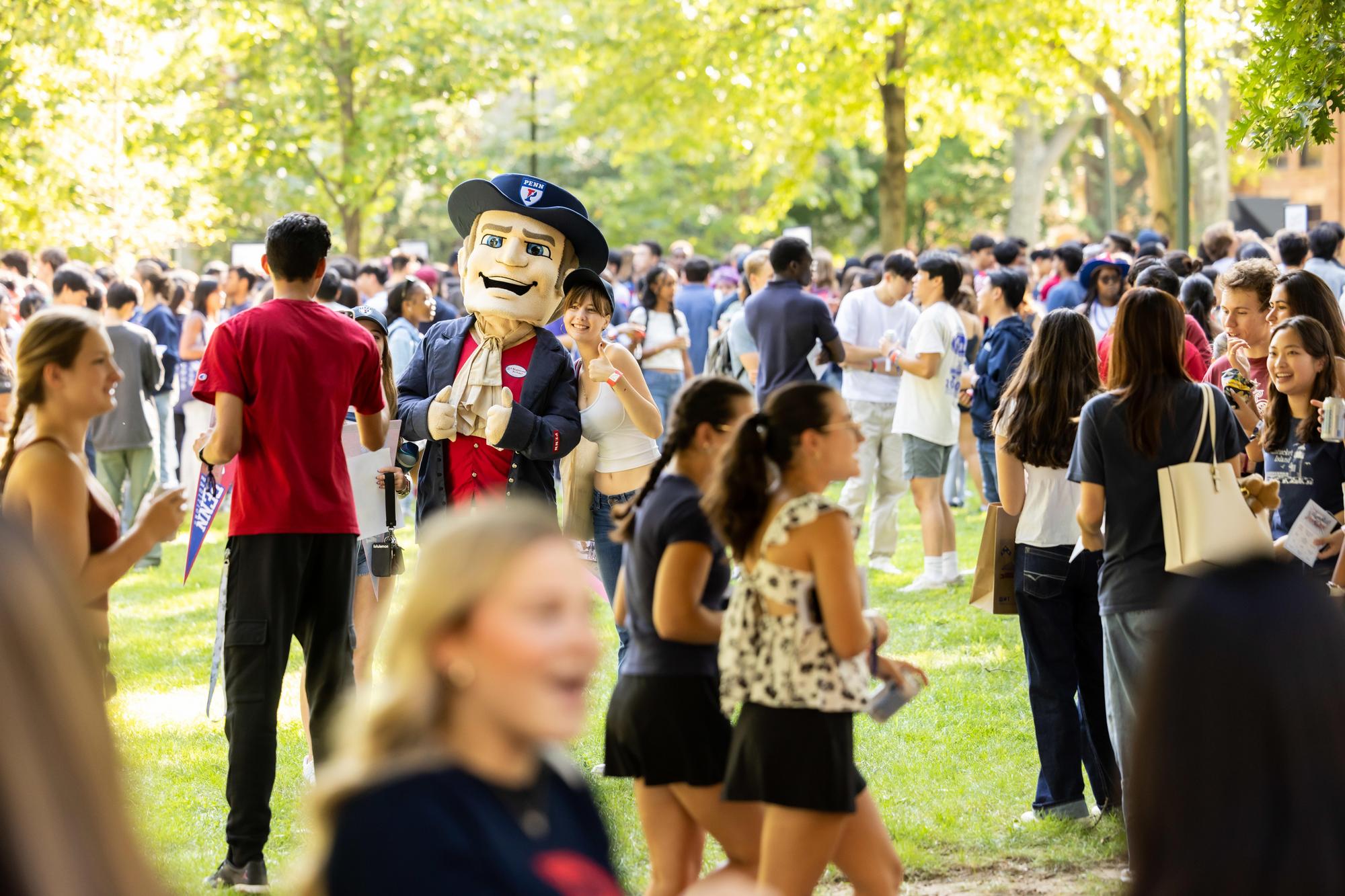 The Quaker mascot on College Green with a crowd of new students on NSO weekend.