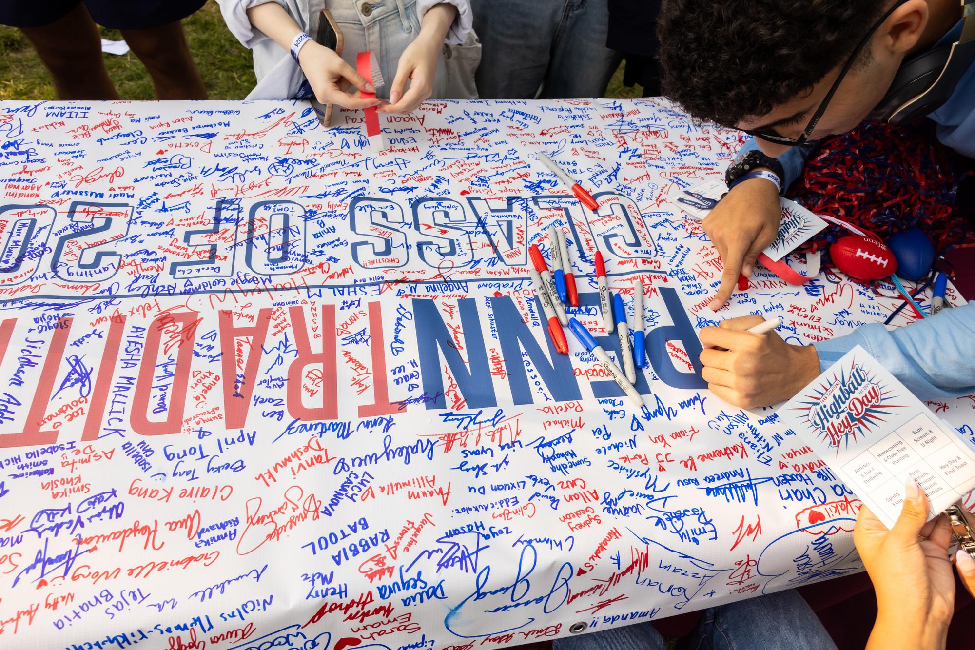 Two students signing their names on a large Penn Traditions Class of 2028 banner on NSO weekend.