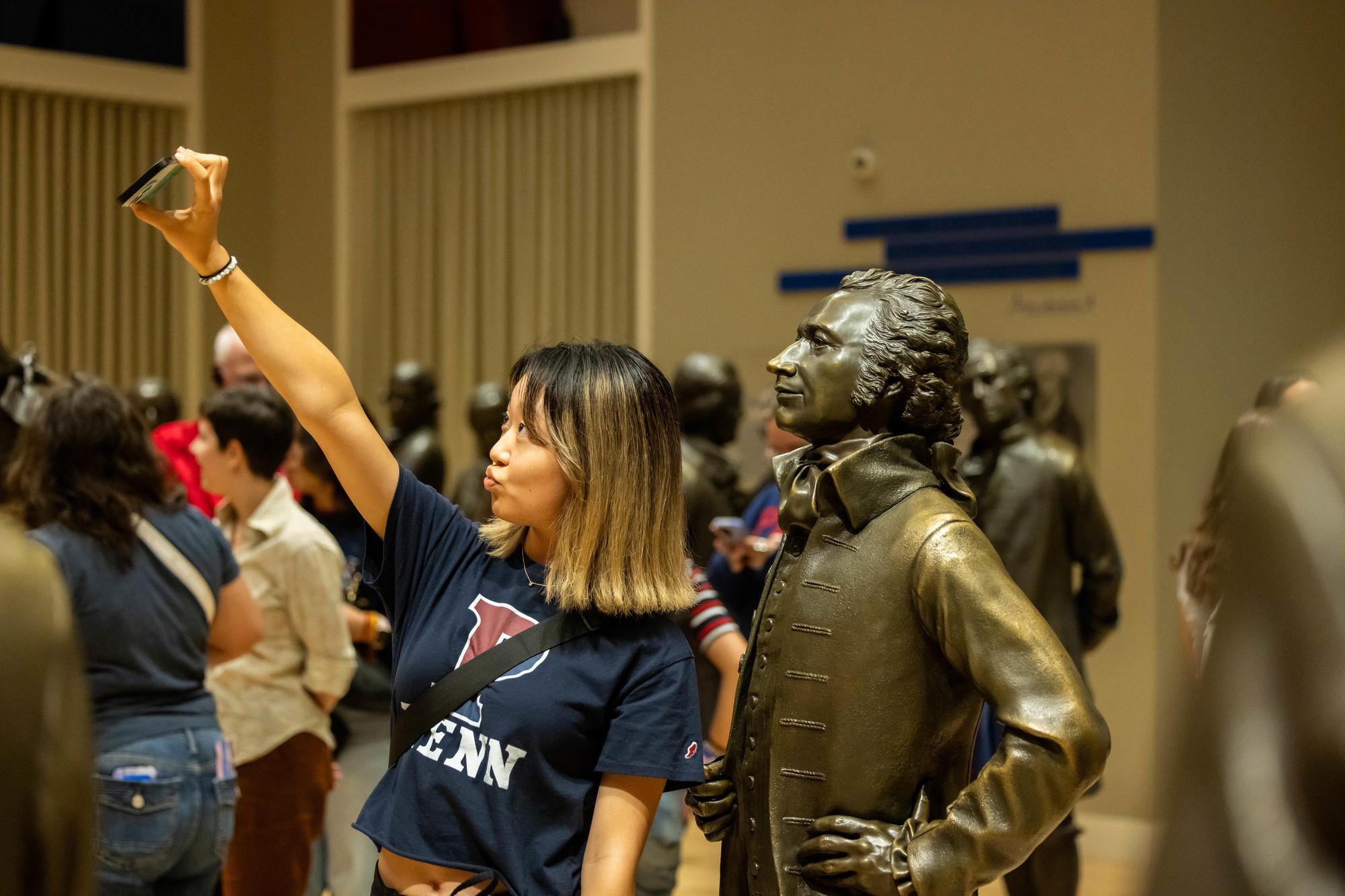 A new Penn student takes a selfie with a founding fathers statue on NSO weekend.