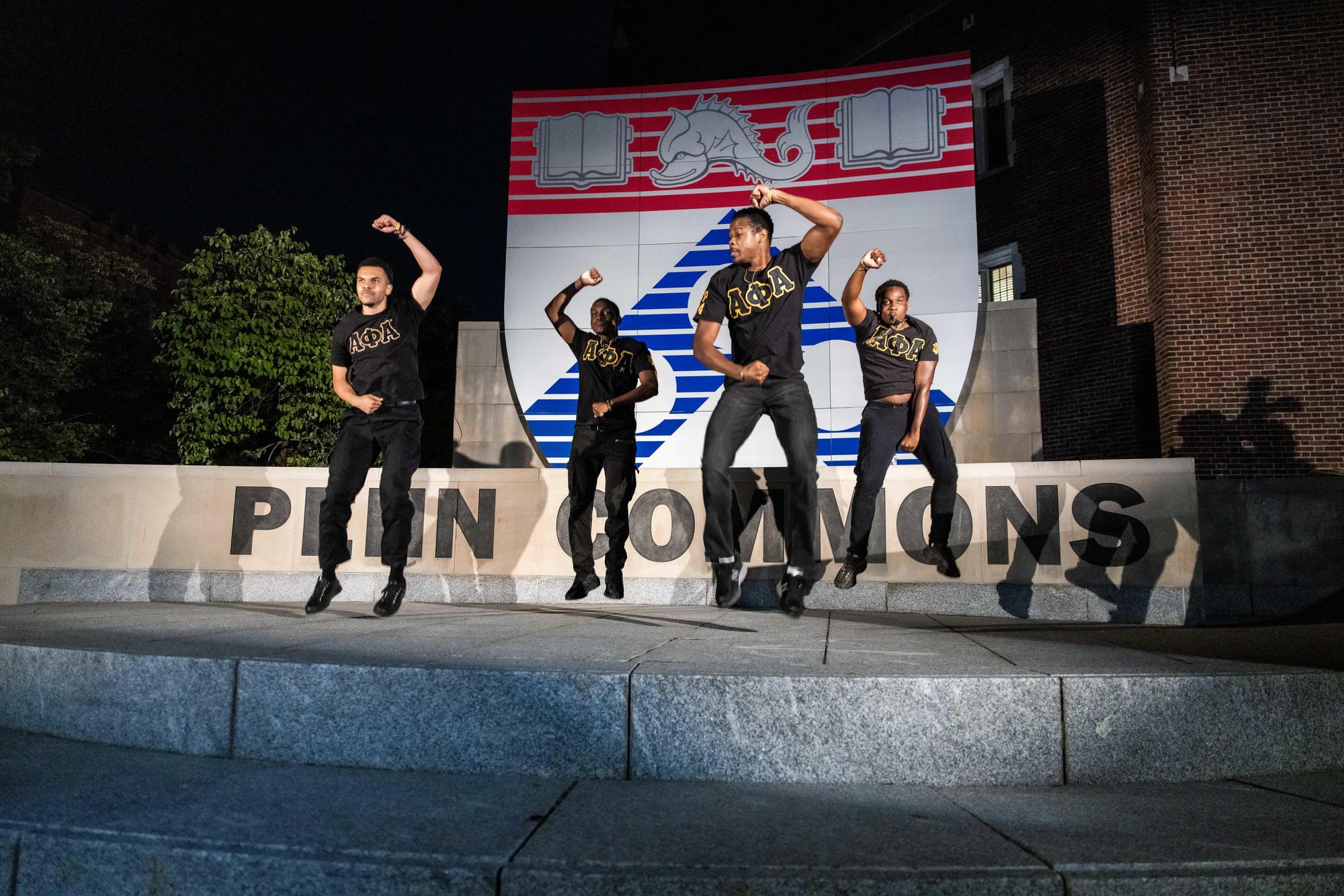 A fourtet of dancers performing at night in front of the Penn Commons sign on NSO weekend.