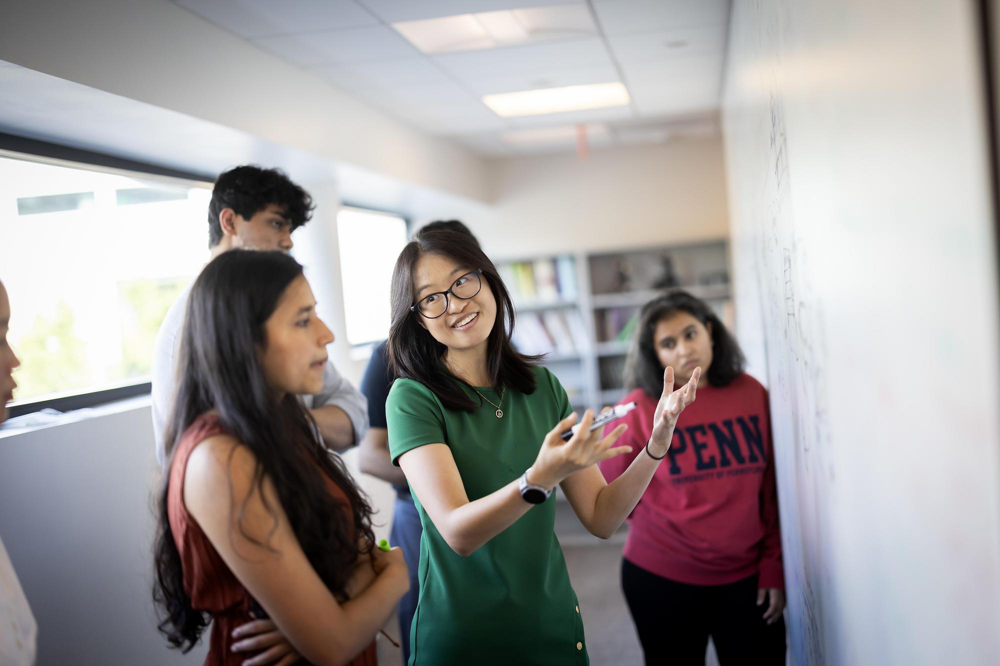 Students gather around a white board to solve a networking problem.